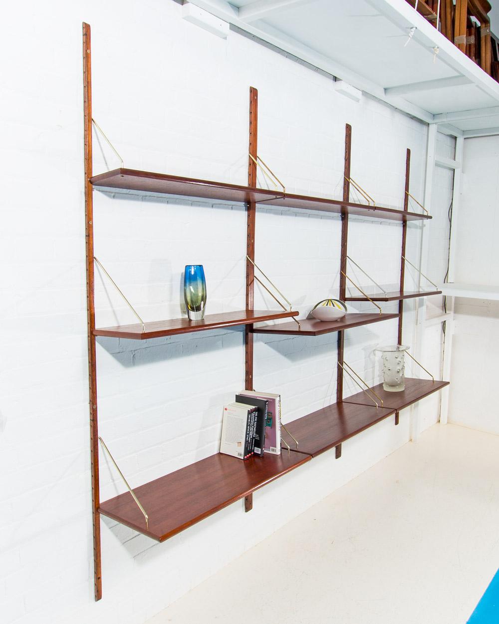 This elegant Danish shelving system features adjustable teak shelves supported by brass brackets, combining functionality with timeless style. The rich, warm tones of the teak wood are beautifully complemented by the sleek brass hardware, creating a