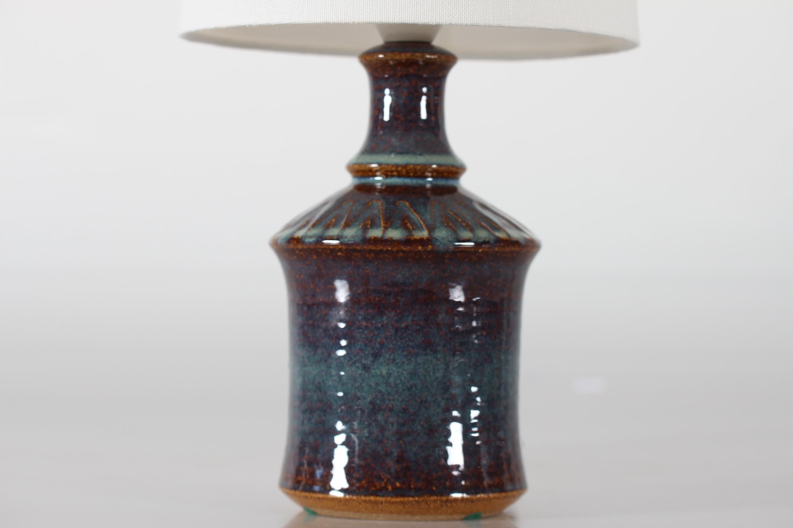 Petite lampe de table en grès de Søholm Stentøj, Danemark, fabriquée vers les années 1960. 
La lampe présente une glaçure brillante dans des tons de bleu, turquoise et brun sur le motif géométrique incisé dans la partie supérieure du pied de la