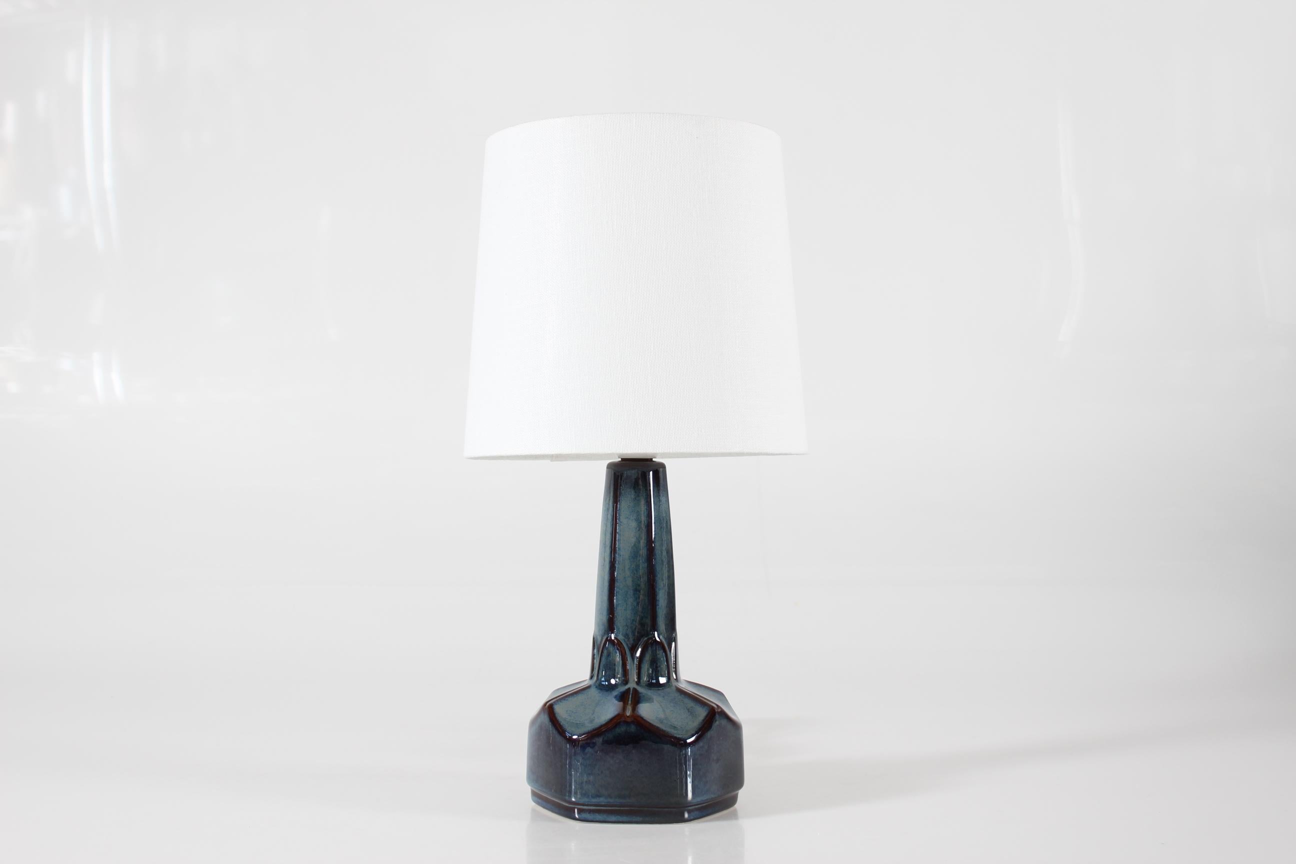 Pequeña lámpara de sobremesa de gres de Einar Johansen para Søholm Stentøj, Dinamarca, hacia la década de 1960.
La forma escultural y el esmalte azul polvoriento brillante, que se vuelve marrón en los bordes, dan a la lámpara una expresión muy viva.