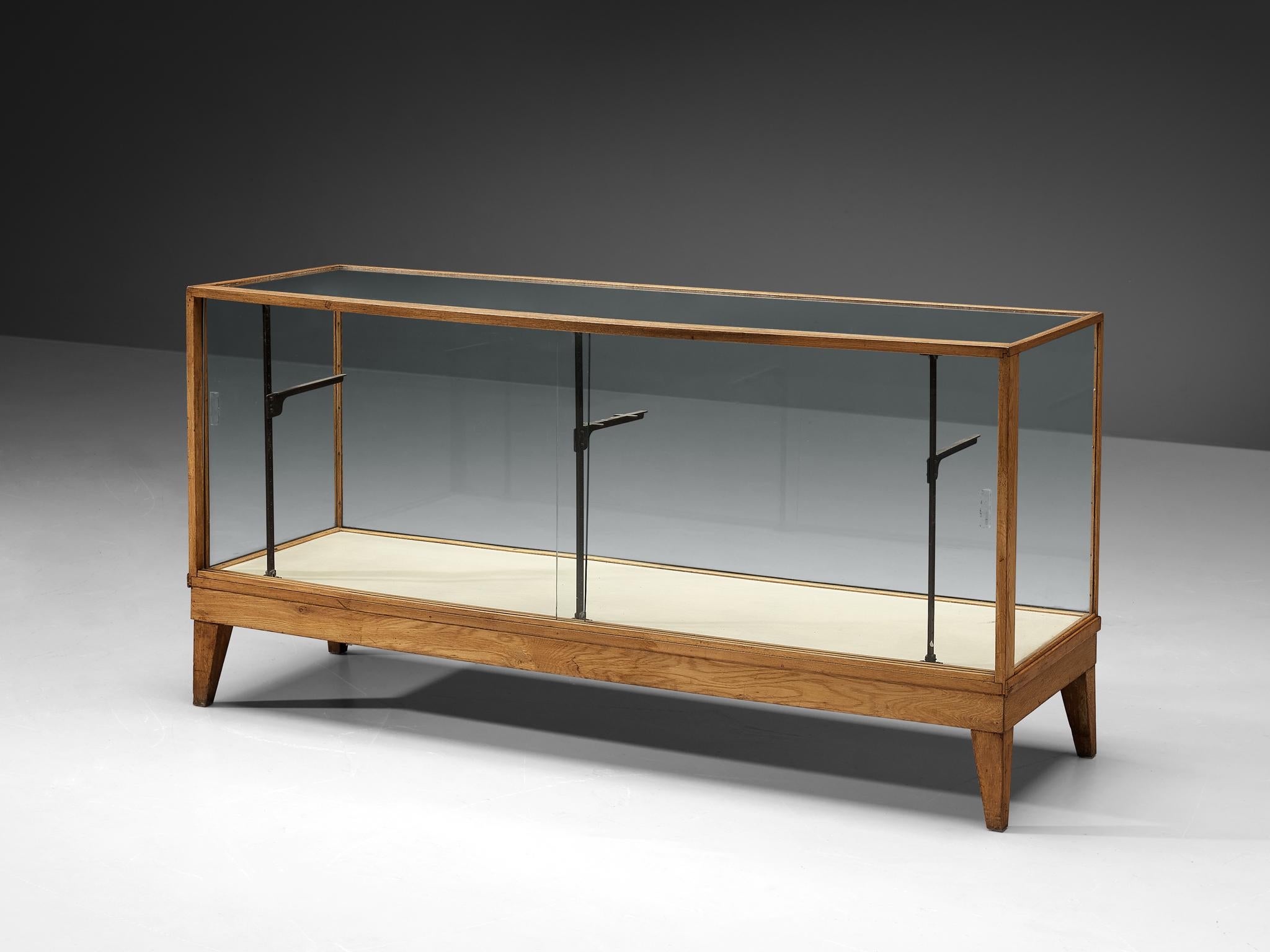 Showcase, oak, glass, brass, Denmark, 1950s. 

Danish showcase with large glass windows and top. Through sliding doors on one side of the showcase, the interior is accessed. Originally the showcase features one glass shelf that can be done upon