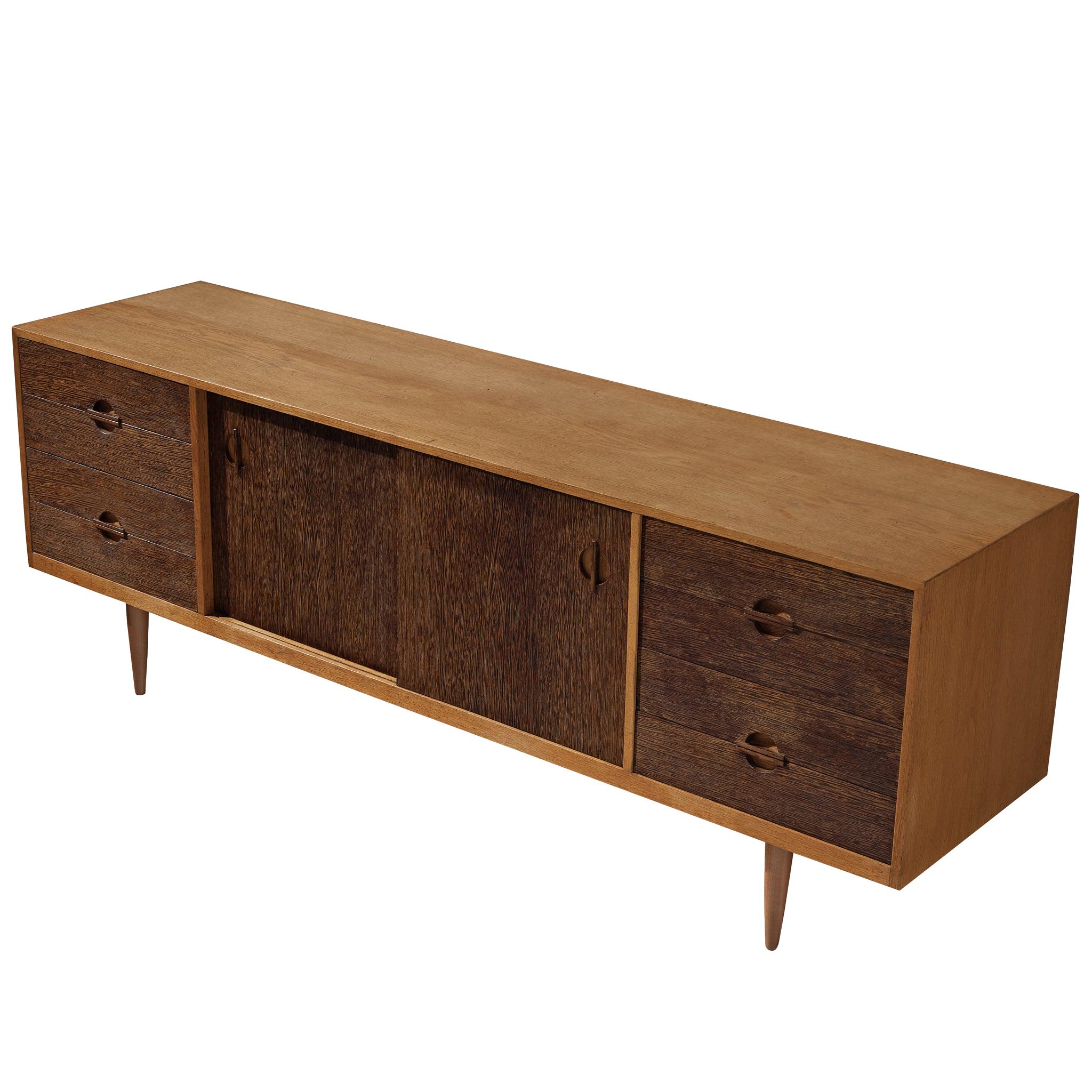 Danish sideboard, wenge, oak, Denmark, 1950s.

This Danish sideboard stands gracefully on tapered, circular legs. A bright frame surrounds the dark fronts of two sliding doors in the middle and two drawer compartments at the side. The handles show