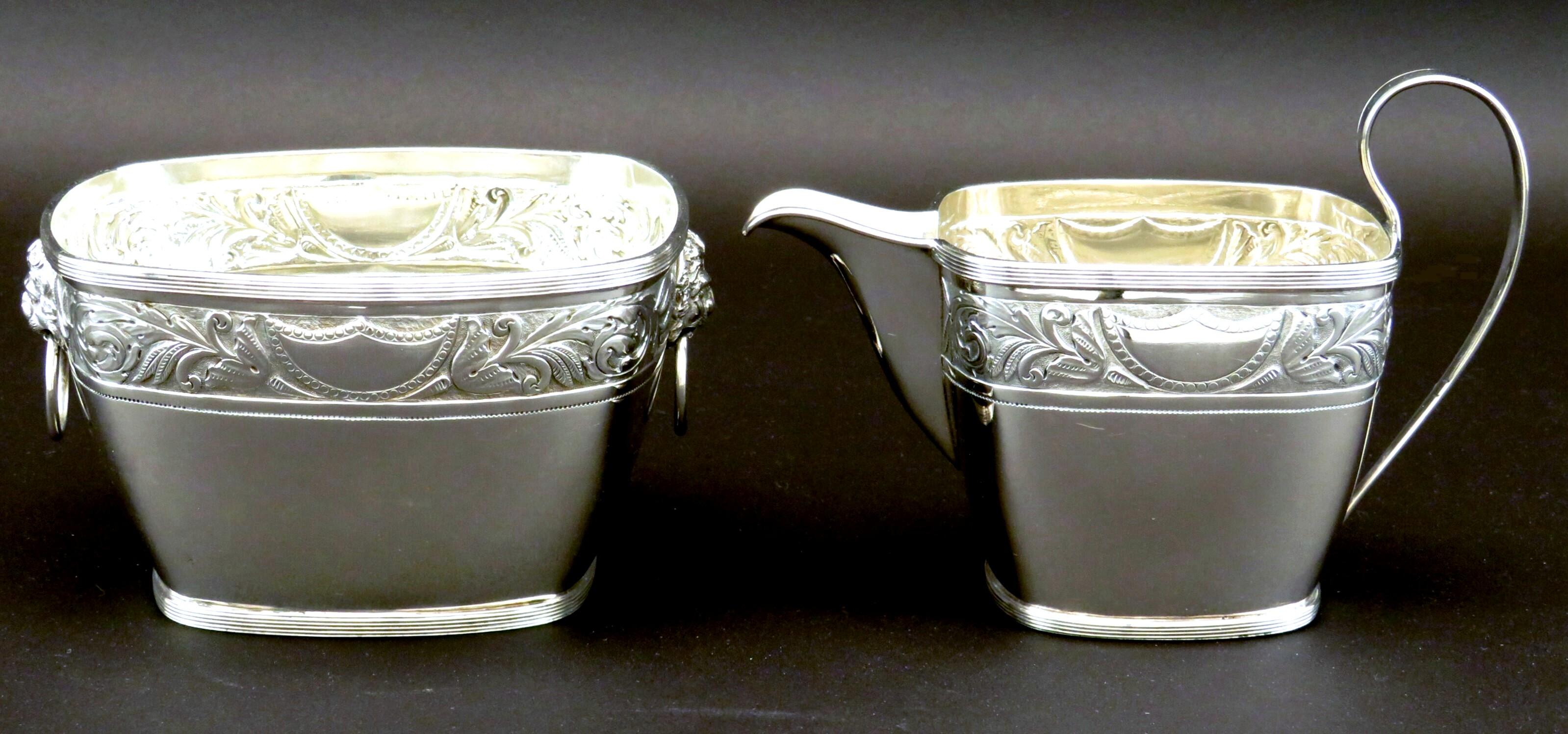 A very handsome Danish silver (.826 Fine) sugar bowl and cream jug of timeless design. Both showing reeded detail to their rims & bases, together with running bands of neoclassical embossed motifs set against a stippled field, interspersed on either