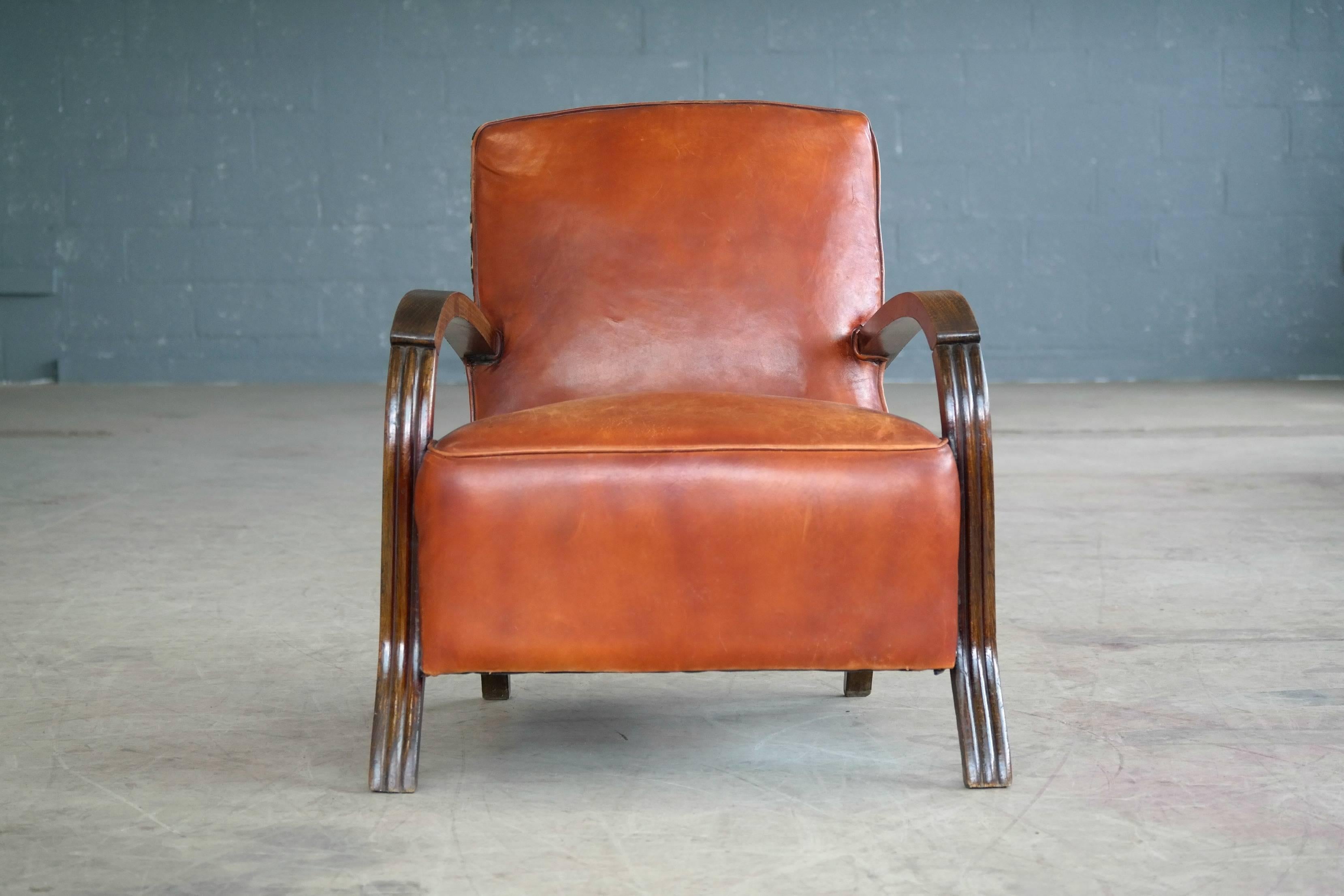 Very charming 1930s small lounge chair from Denmark. Carved wooden armrests in stained beech showing some nice patina and age wear. The chair has been re-upholstered in a nice aniline cognac colored leather at a later point with nice brass tack