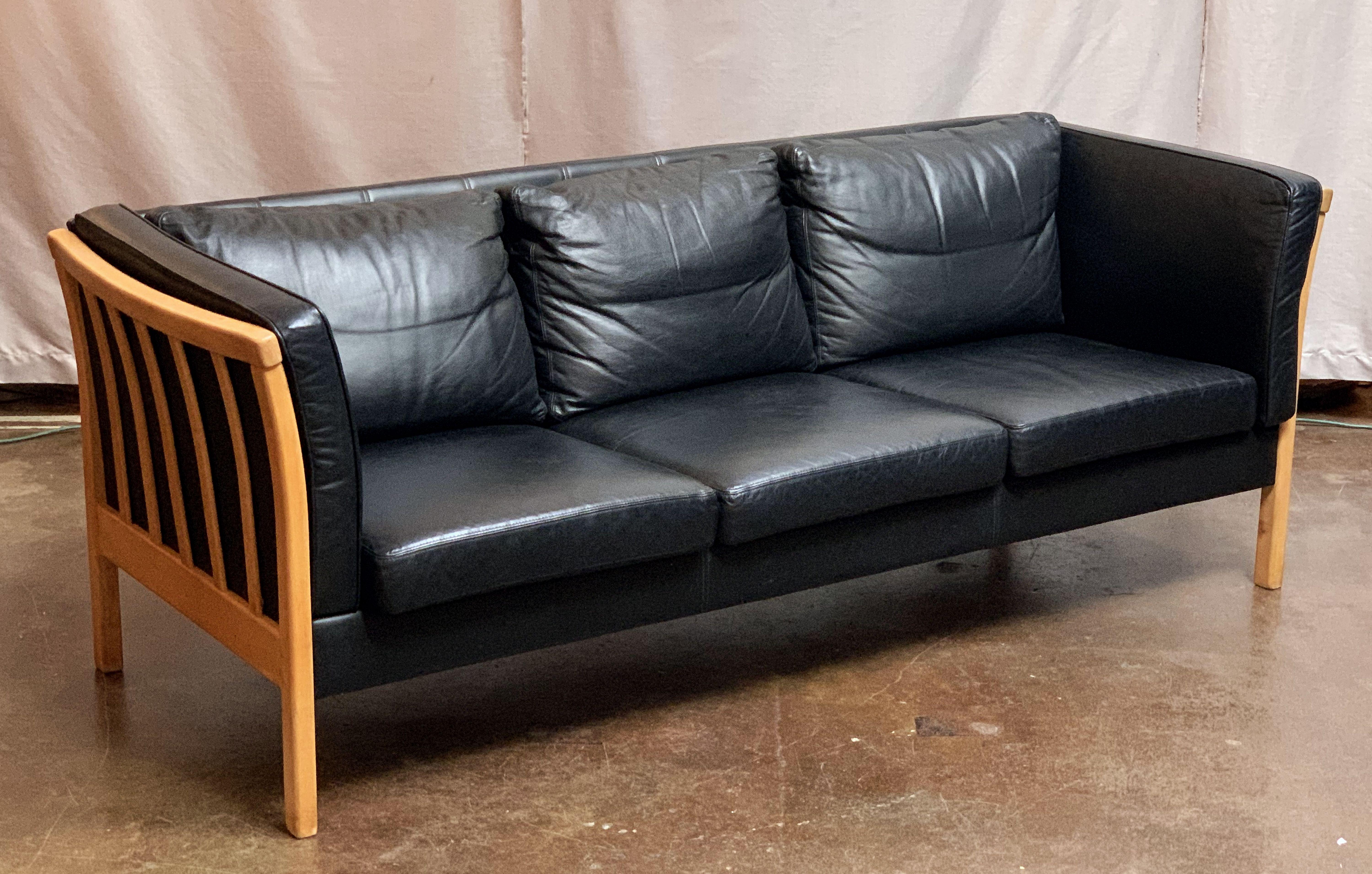A period Danish modern three-seat upholstered sofa or settee (couch) of black leather and beech wood with handsome, stylish design by the celebrated design studio, Stouby.

Featuring eight cushions (seats, back, and sides) on a stylish upholstered