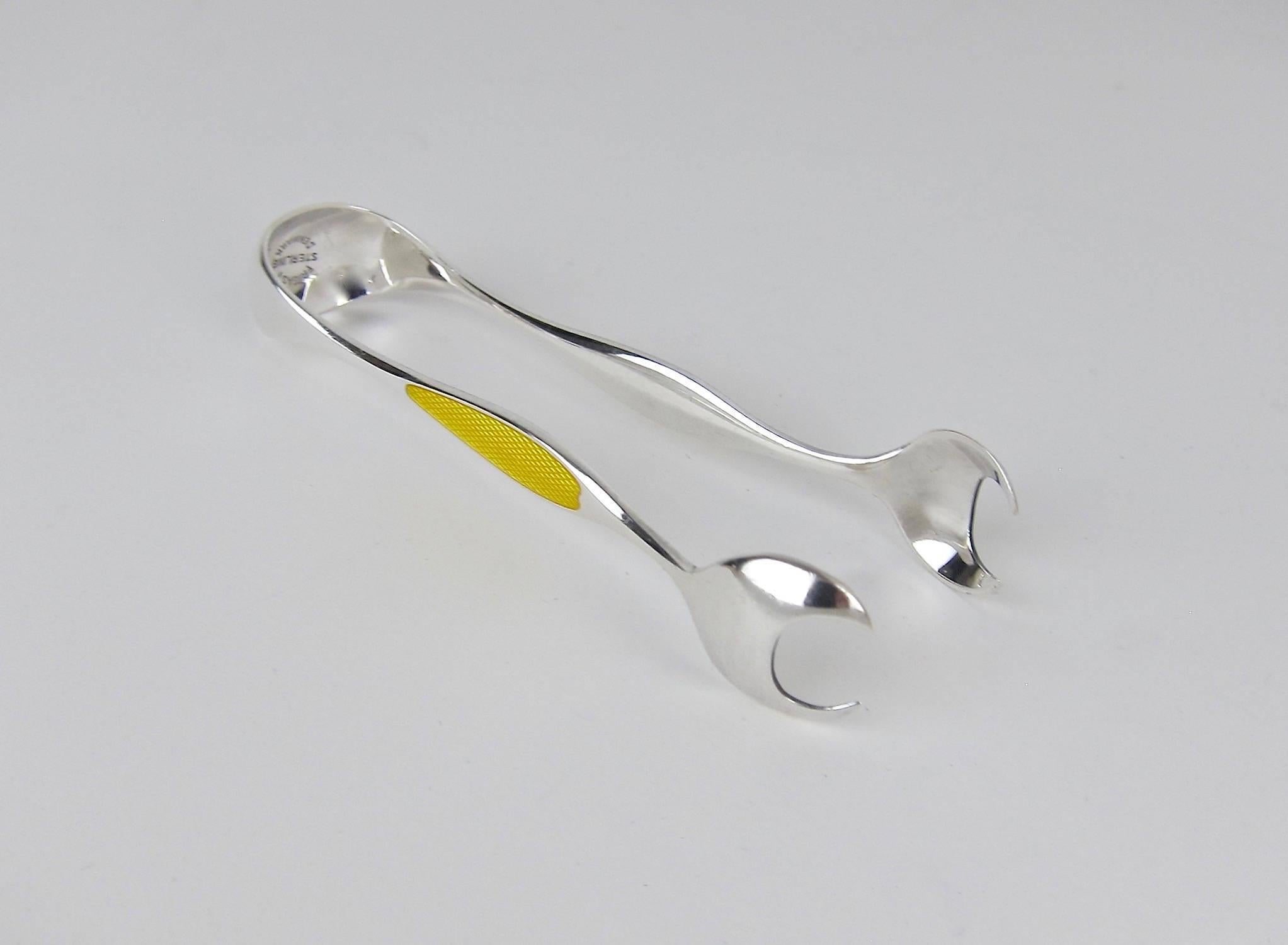 A vintage pair of sterling silver tongs decorated on either side with a contrasting panel of guilloche enamelling in golden yellow, made by Frigast Silversmiths of Copenhagen, Denmark, active 1958-1976.  The silver tongs are in very good condition