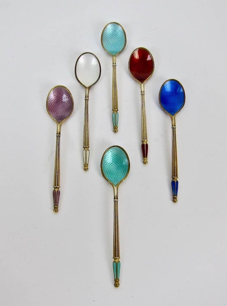 A boxed set of six sterling silver gilt spoons decorated with jewel toned guilloche enameling from Anton Michelsen of Copenhagen, Denmark, circa 1960s.

Each solid silver spoon has a gold wash and colorful enamels ornamenting the finial, front and