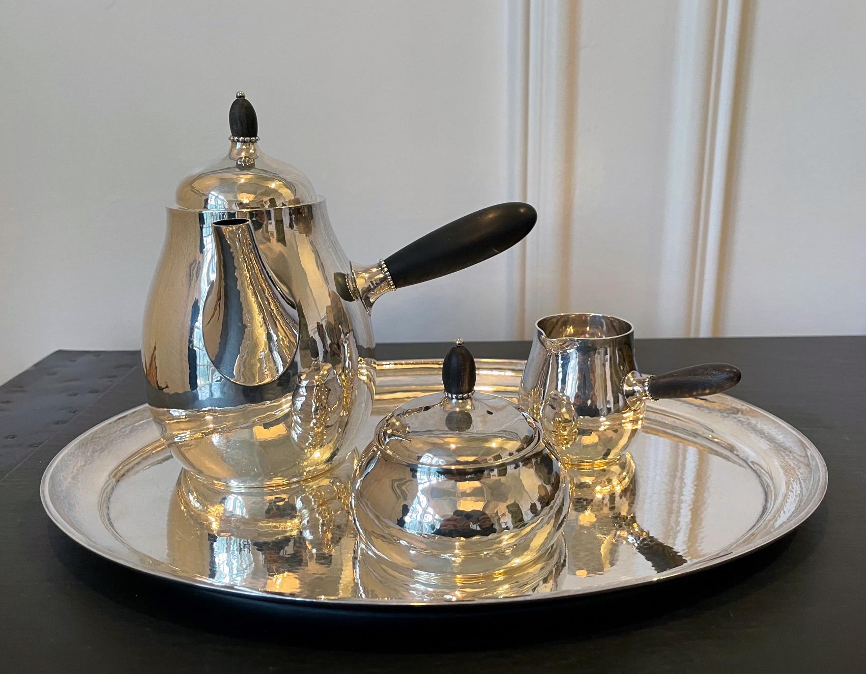 A Danish sterling silver four-piece coffee or tea set by Georg Jensen. This lovely set consists of a coffeepot, lidded sugar bowl, creamer, all of Models 80A, with a hammered silver tray model 223C. All piece bear GJ marks of post 1945. Model 80,