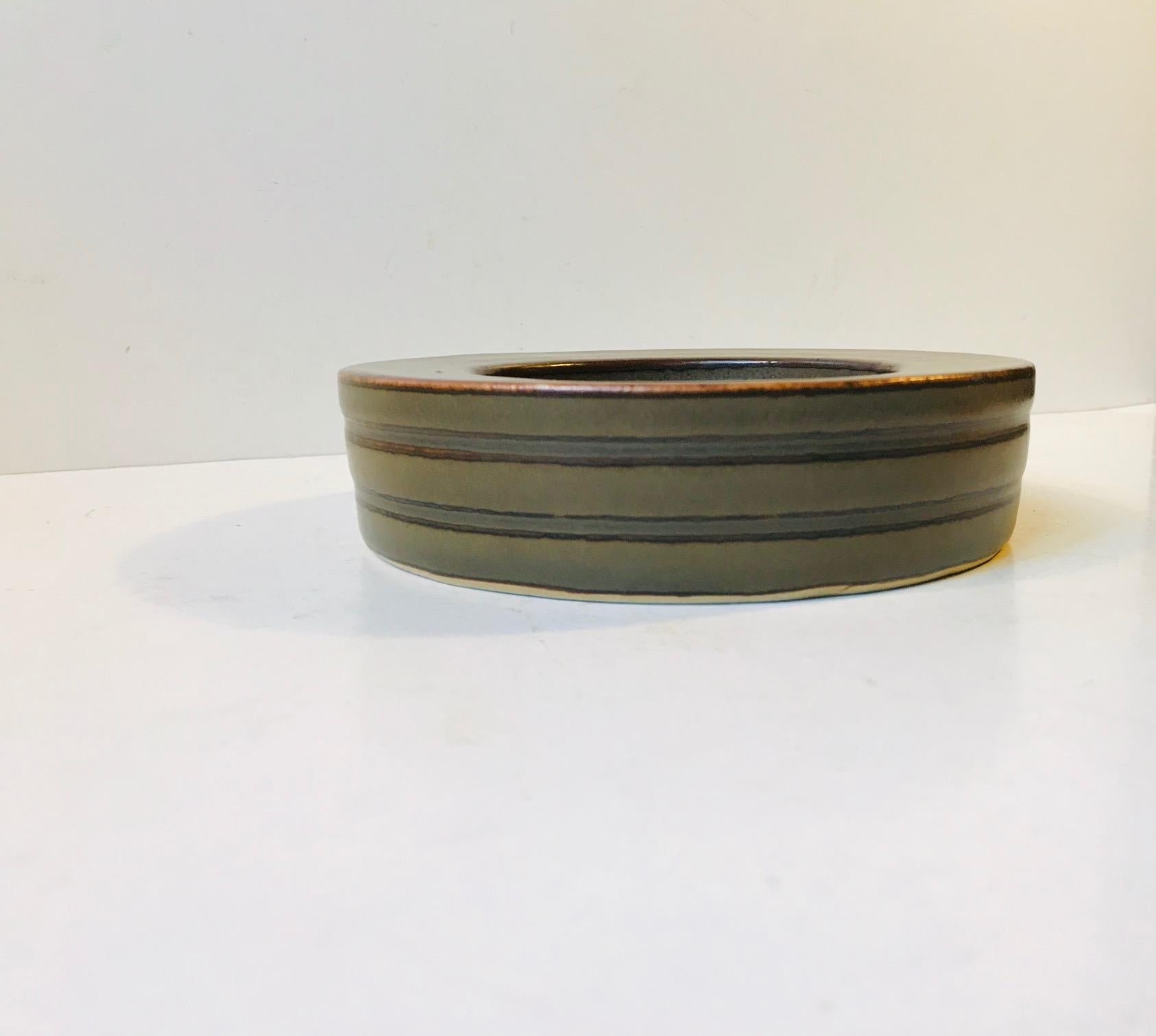 This circular heavily glazed earthy textured stoneware bowl is designed by the Danish ceramist Valdemar Petersen and manufactured by B&G. It is signed by the artist and maker at the bottom. The glazing techniques applied are reminiscent of Nils
