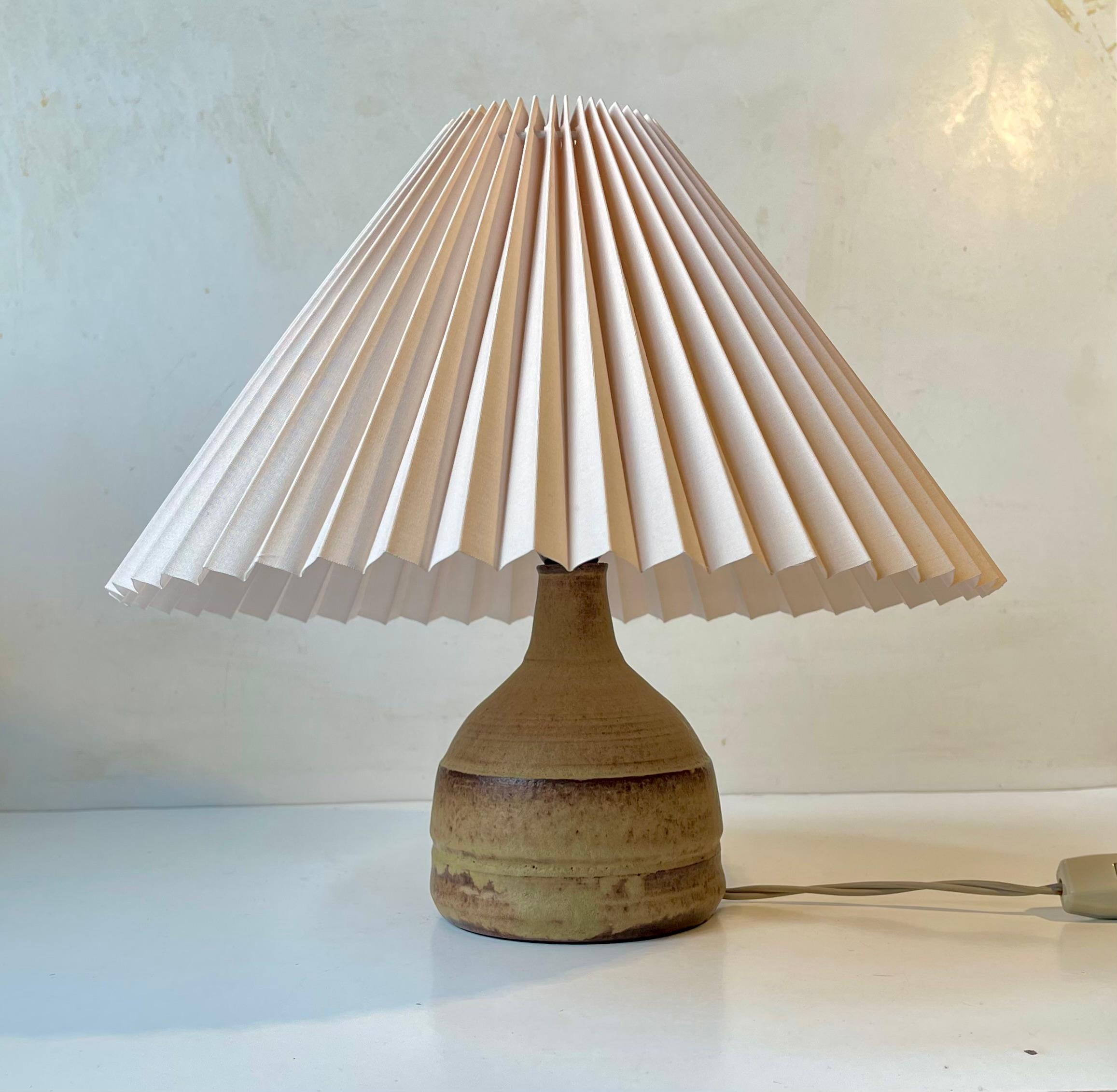 Élégante lampe de table en grès en forme de maillet avec abat-jour danois beige cannelé. La base présente des glaçures terreuses délicates aux nuances douces. Conçue et fabriquée anonymement au Danemark vers 1970.   

Dimensions : H : 35 cm,