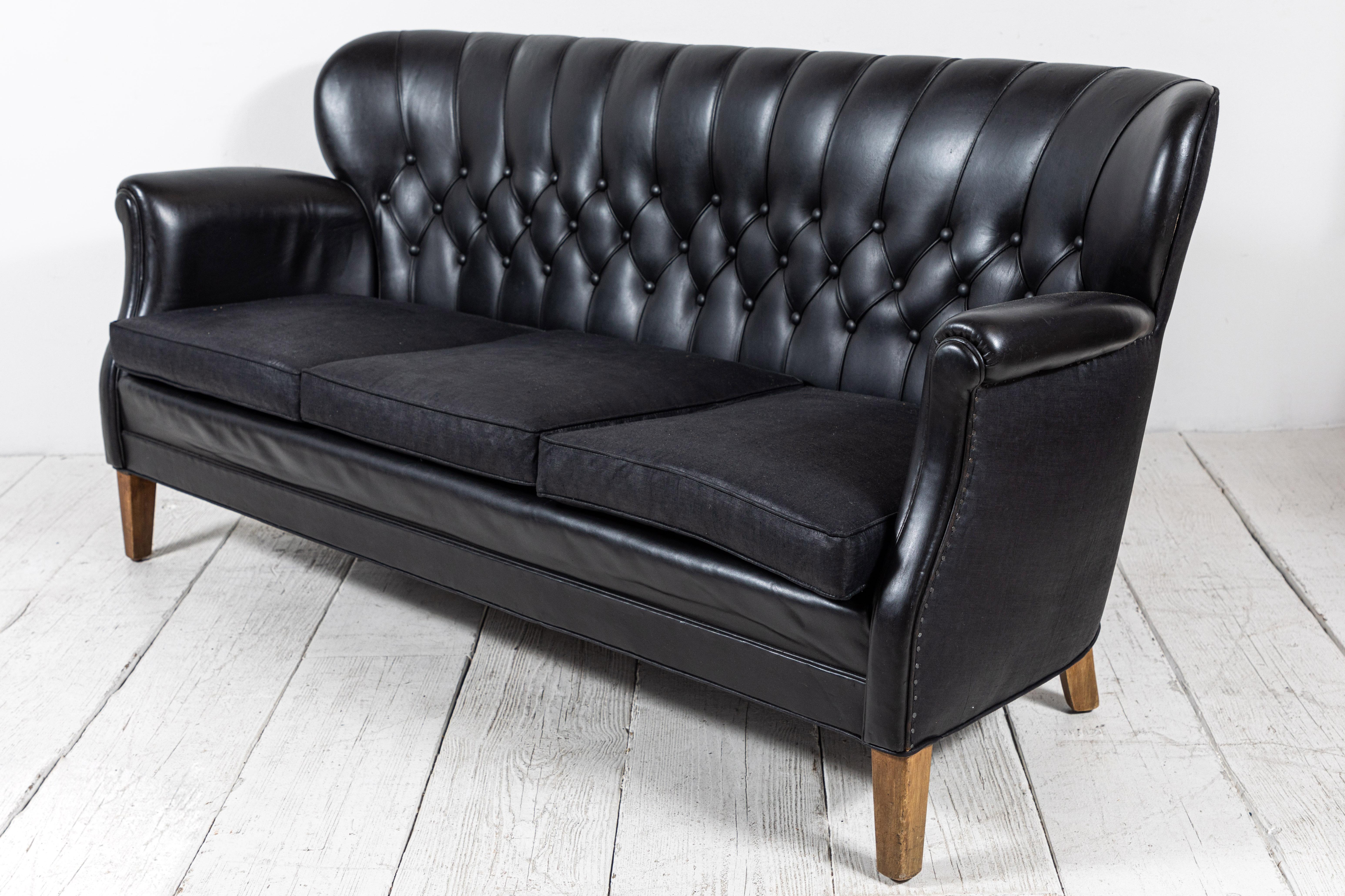 Danish style leather tufted settee with slight winged sides. Black beetled linen applied to the back seat cushions.