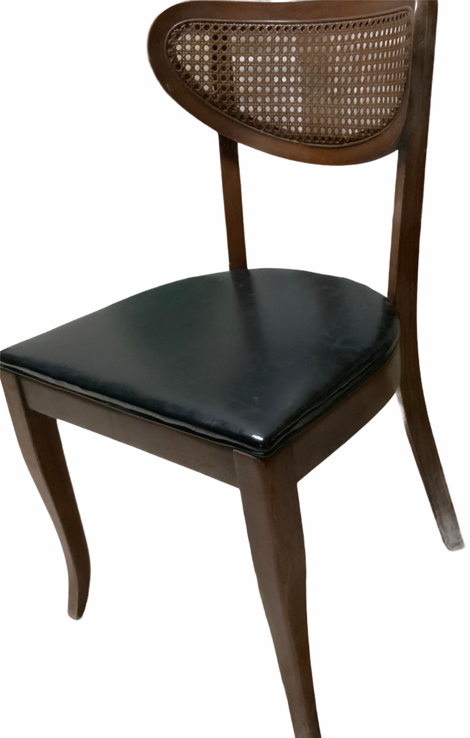 This is a danish style solid wood chair. It’s back is elliptical shaped and made of a caned net. The seat is a wide“D”shaped one and is upholstered with black leather like fabric. The chair is supported by two four sided tapered legs in the back and