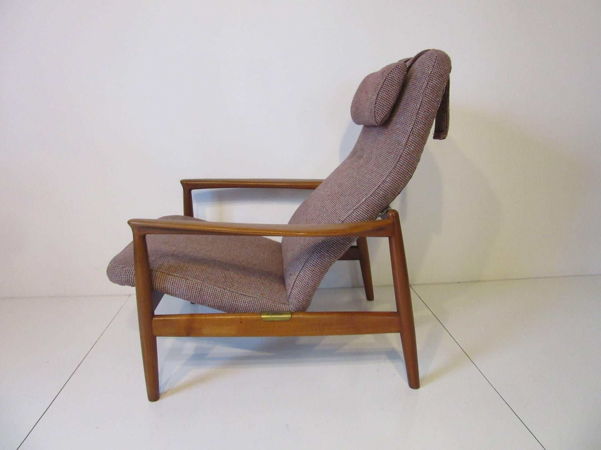 A Danish styled teak wood framed lounge chair with contoured sculptural arms and seat designed for comfort, hanging head rest pillow all upholstered in a tight woven maroon, cream wool blend with flecks as seem in the photos. Retains the