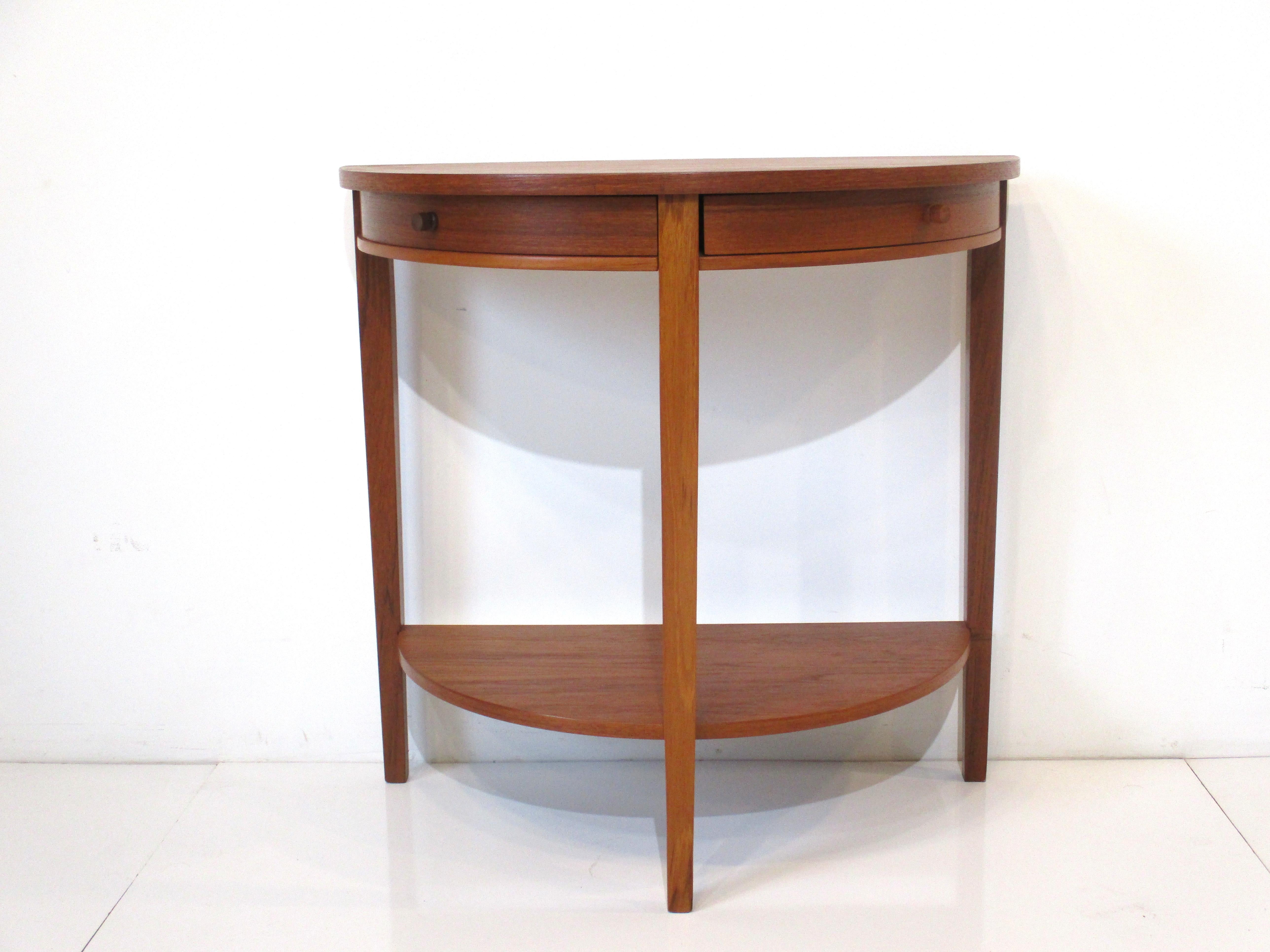 A wonderful half moon shaped hall or entrance way teak table with two drawers that neatly swing out having turned teak knobs. Siting on three sturdy legs and having a lower shelve handcrafted by Otmar known for his detail and finely designed pieces.
