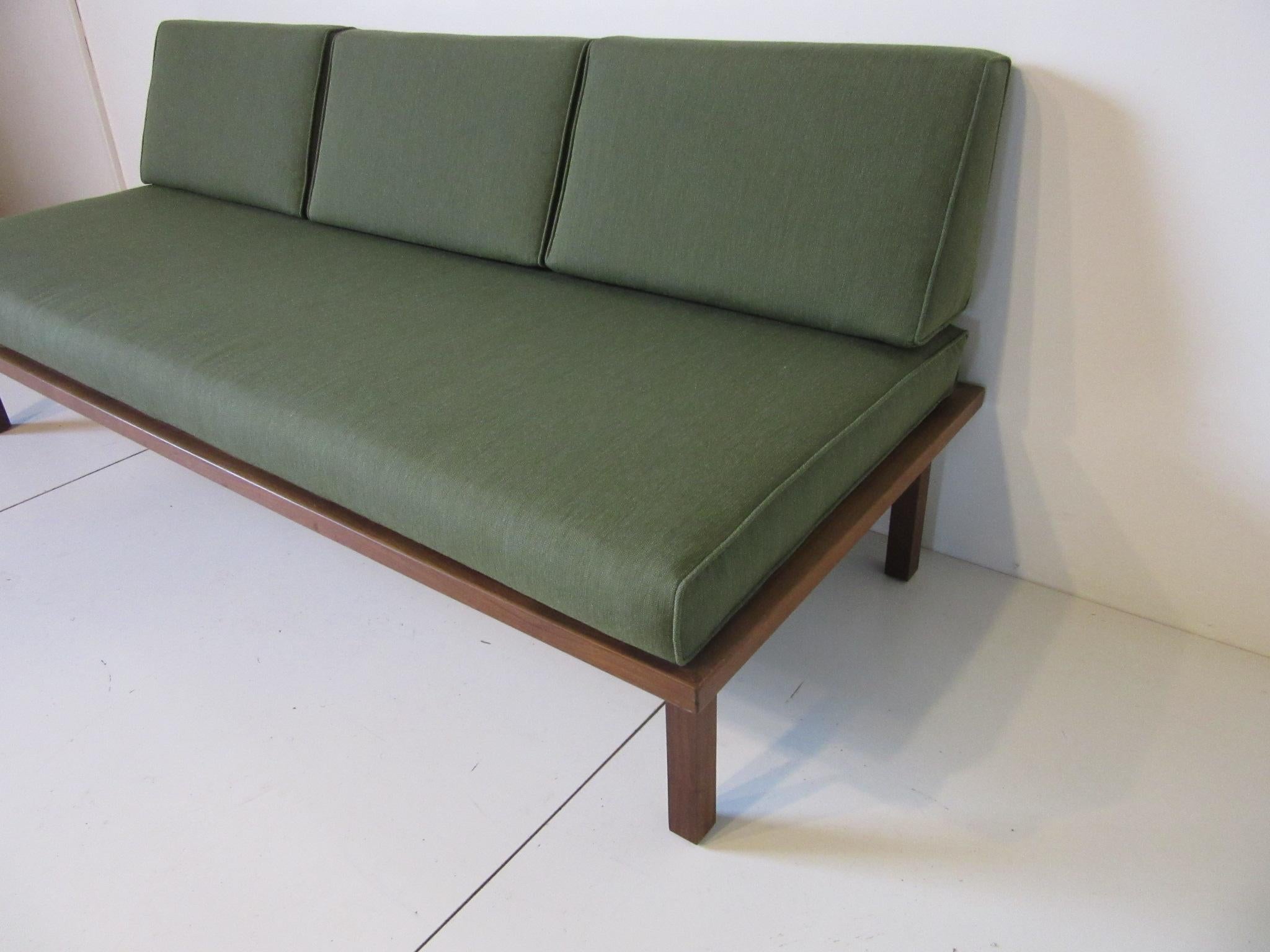 A Danish styled daybed or sofa with upholstered bottom and three loose back cushions in a green blended fabric. With no back rail this is perfect for that smaller living space or that spare room for a guest, also having folding legs that lock so it