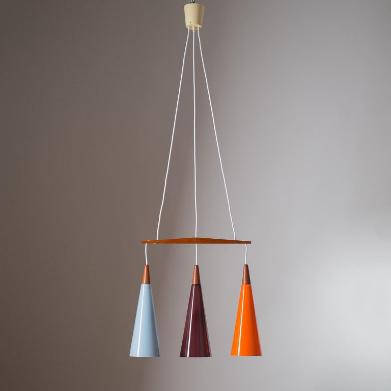 Rare colourful Danish glass and teak chandelier by Holmegaard, 1960s. Three blown glass cones of different color are suspended from a 'floating' teak bar. Each cone has one E27 socket with new wiring. Overall height is adjustable up tof