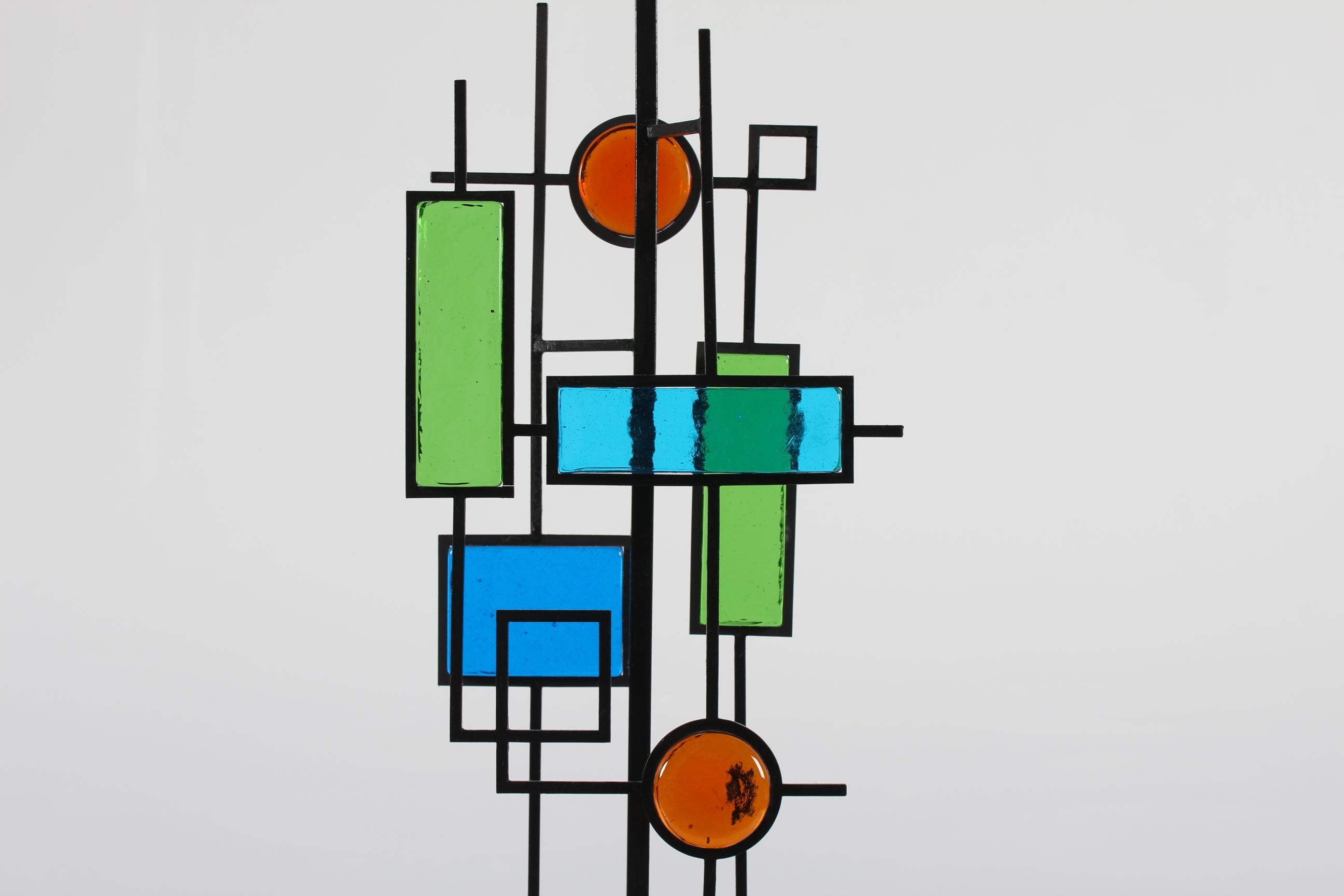 Grande lampe de table conçue par le danois Svend Aage Holm Sørensen (1913-2004).
Le pied de la lampe a un cadre en fer laqué noir. Insérées dans le cadre, des mosaïques géométriques en verre de couleur bleue, verte et rouge. La base carrée du pied