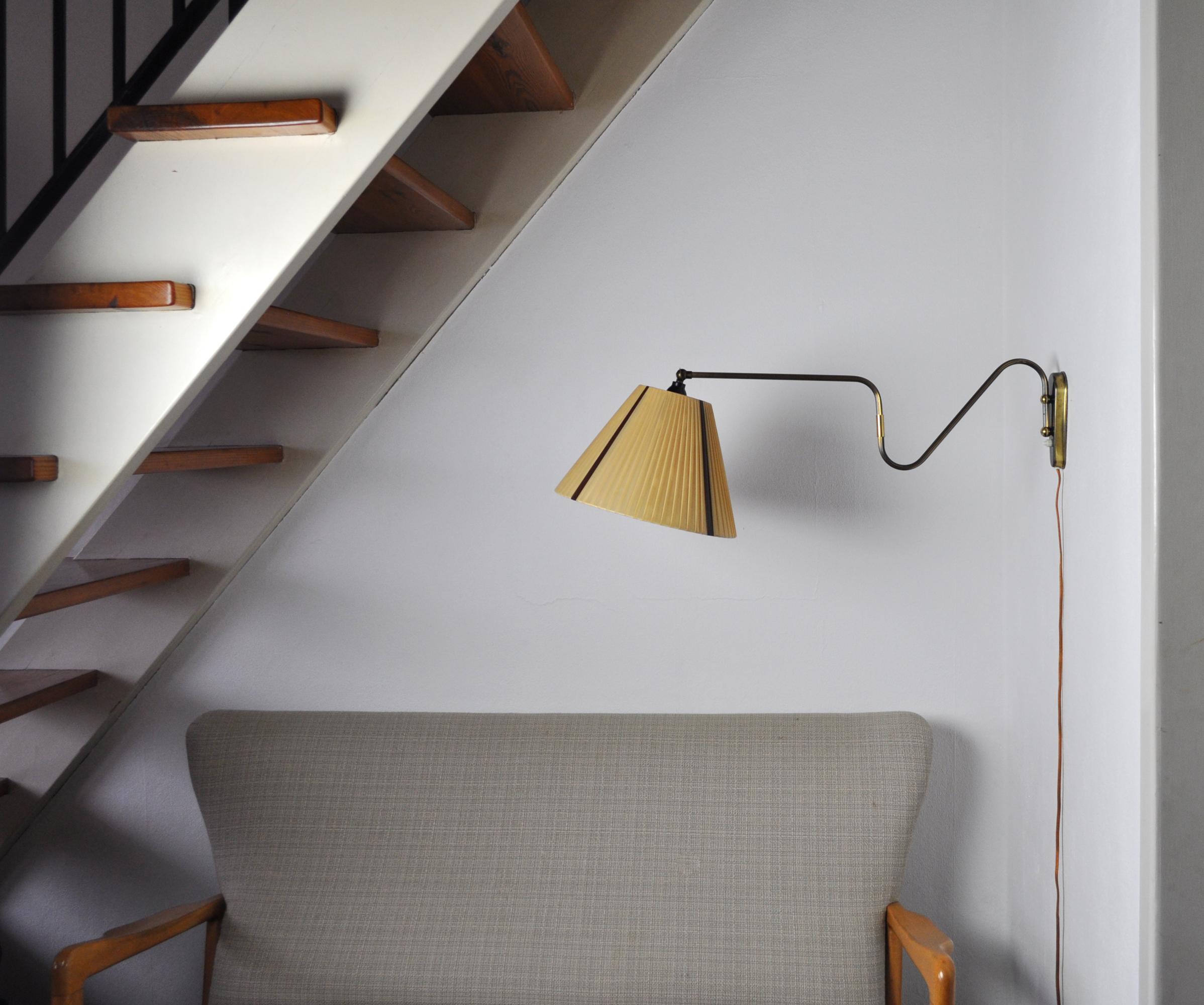 Brass wall lamp with two-piece swing arm and adjustable head.
Swivel and wall mount made in brass, mounted with original shade in mustard color and four brown stripes. 
Probably made by Lyfa, imprinted on the plug.

Measures: Arm length incl.