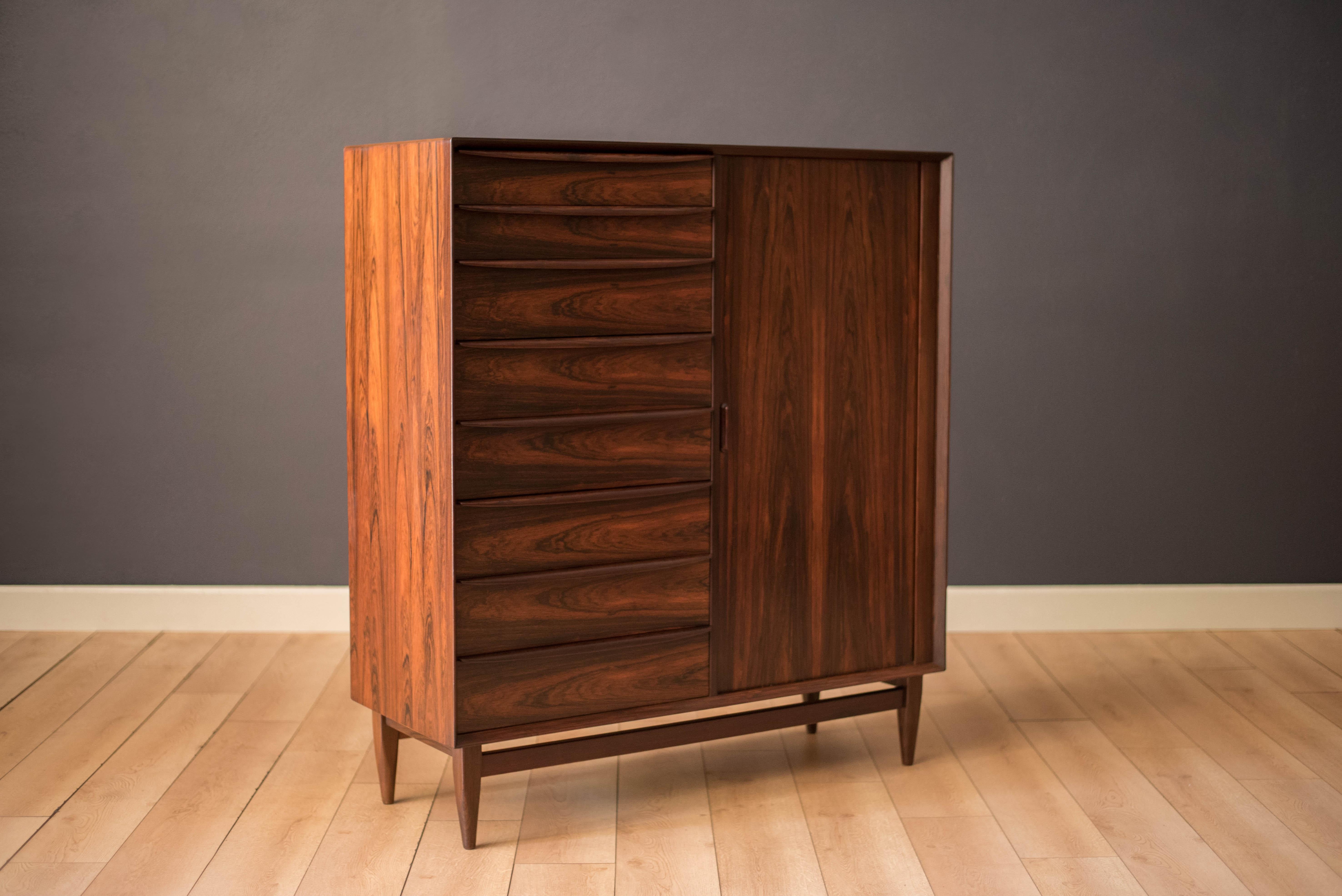 Mid-Century Modern highboy dresser chest in rosewood designed by Svend A. Madsen for Falster Møbelfabrik, Denmark. Features eight dovetailed storage drawers with sculpted pulls and a sliding tambour door that reveals an additional nine
