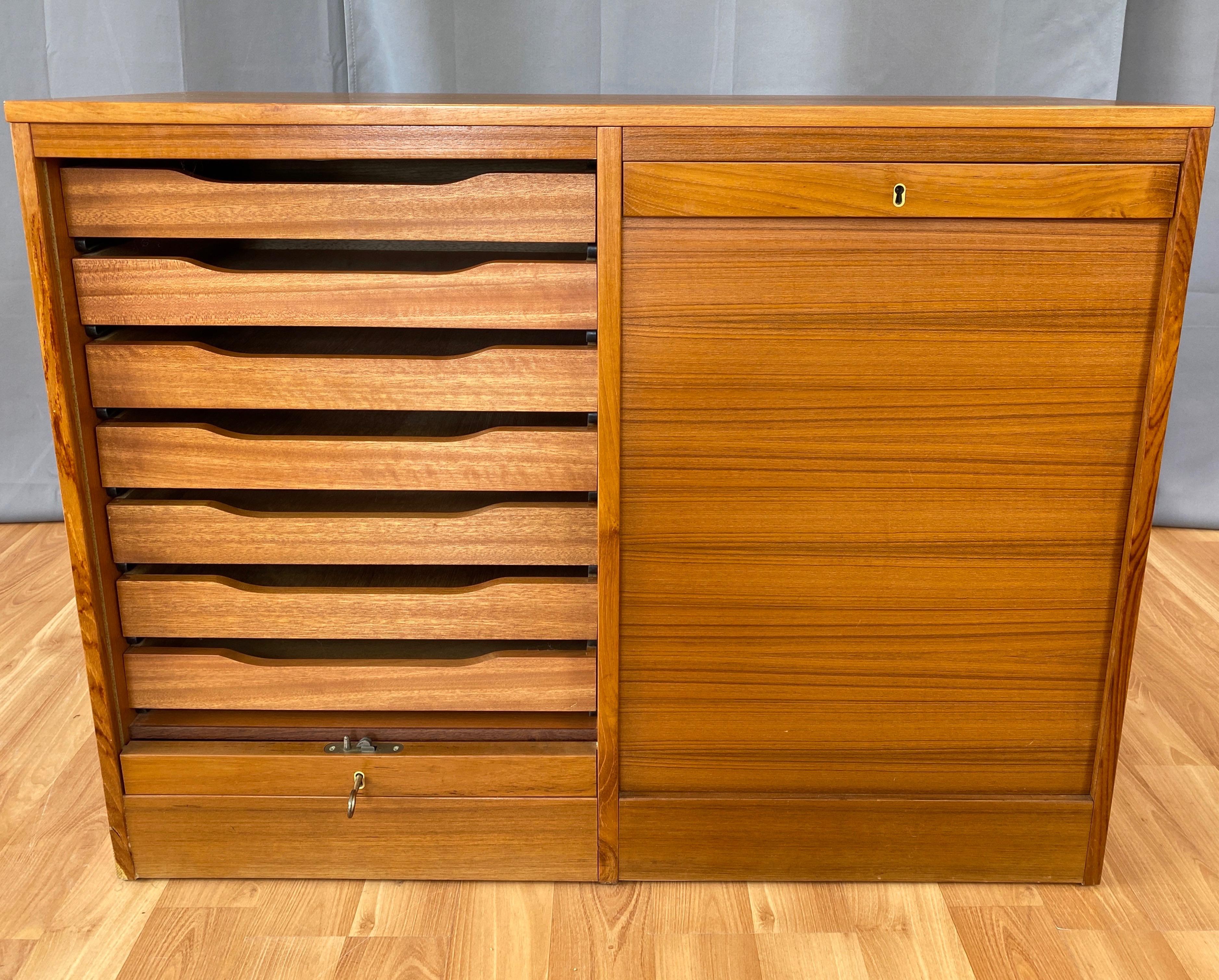 A 1970s Danish modern dual compartment teak file cabinet with drawers and locking tambour doors.

Clean and compact design features smooth-front tambour doors that slide down into the base and out of sight. Each compartment holds seven drawers