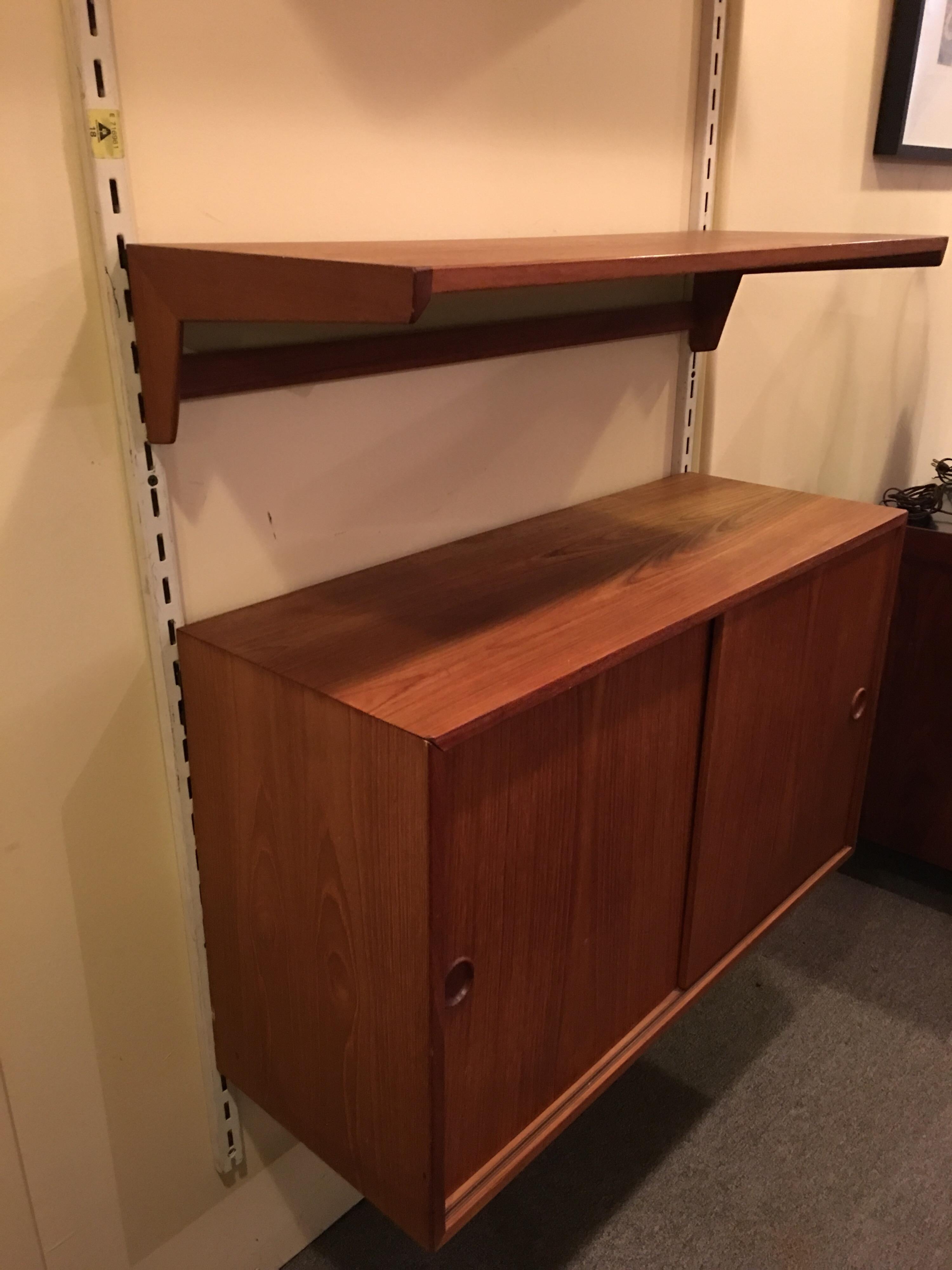 Danish teak adjustable shelving system with sliding door cabinet. Stamped Made In Denmark. Shelves and cabinet may be placed anywhere on the 69 inches of stanchion and they are 33.75 inches in width and 12.5 inches deep.