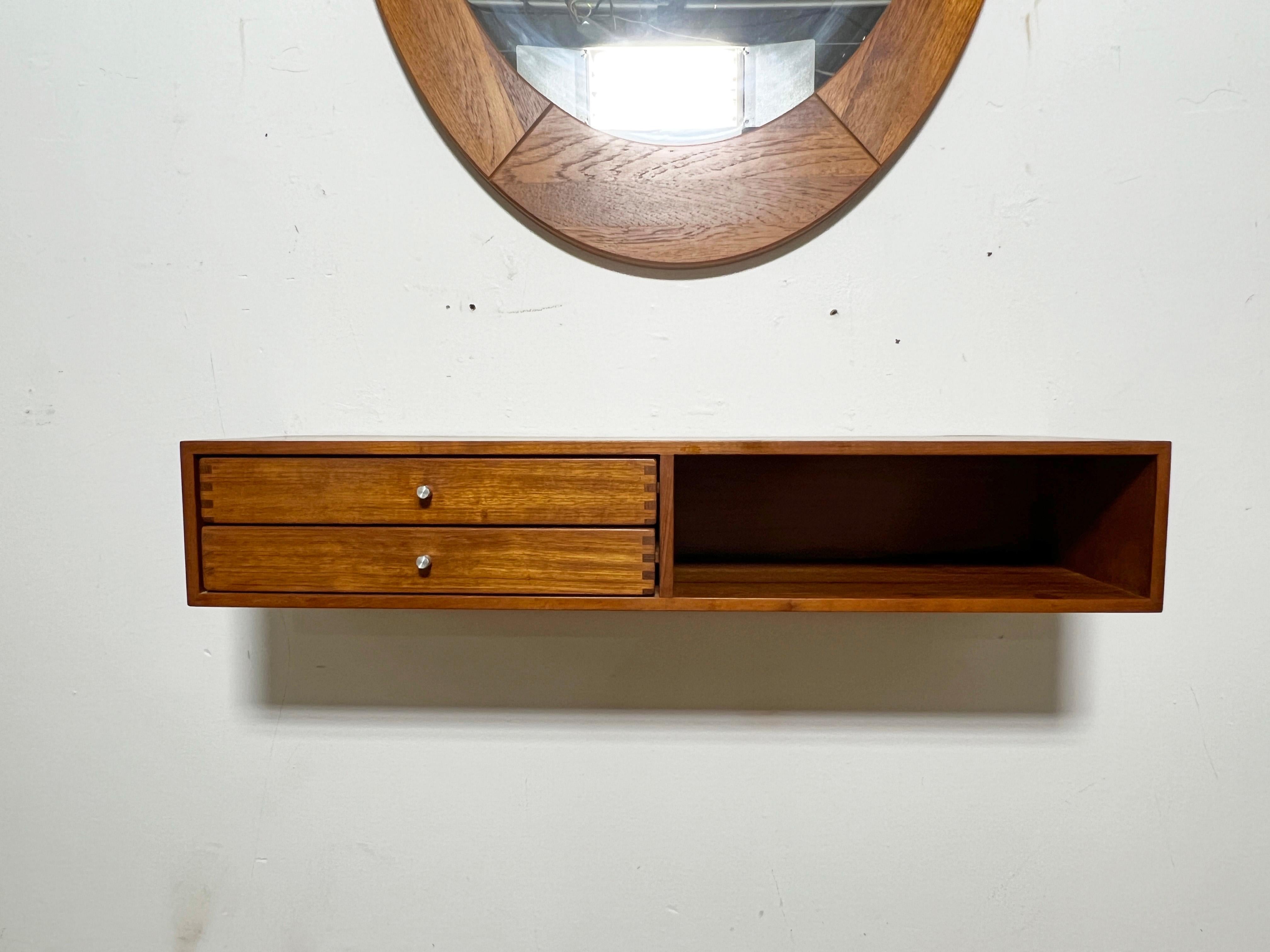 A Danish teak floating wall mounted console with two drawers by Aksel Kjersgaard, paired (as found in the estate from which it was obtained) with a large teak oval mirror by Pedersen & Hansen. 

Console measures 35