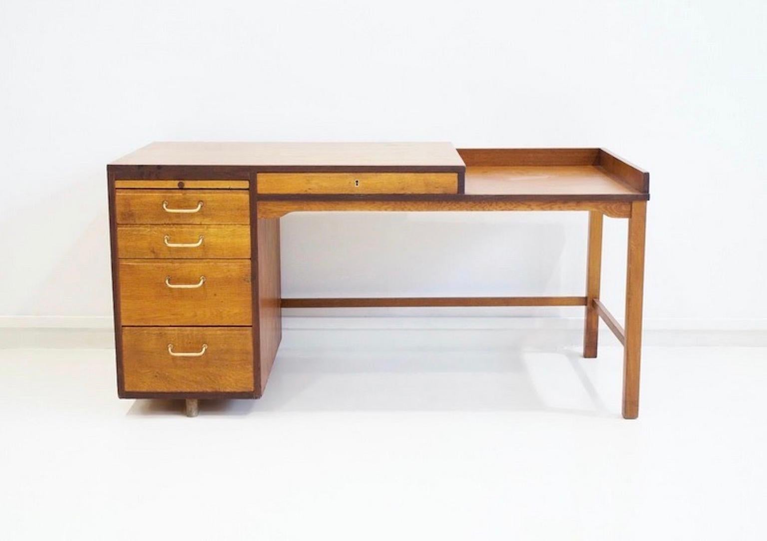 Scrivania in teak impiallacciato e rovere massiccio. Quattro cassetti sul lato sinistro, cassetto con serratura al centro. Alcune tracce di usura sotto forma di graffi e segni. Chiave inclusa.