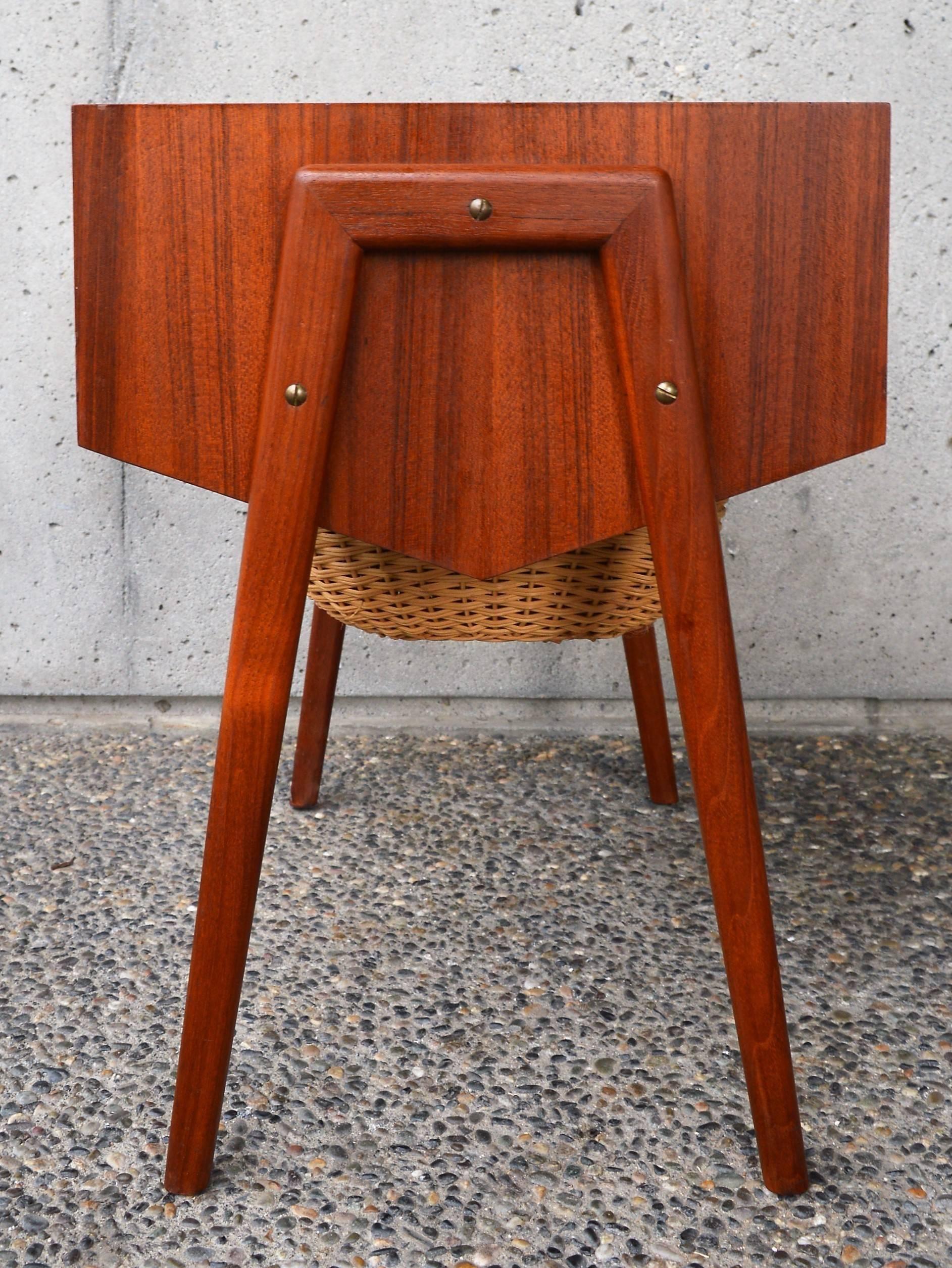 This fun Danish modern teak side table has awesome style and design. Featuring a drawer with segmentations that can be opened from either side, as well as a storage basket on a lower shelf. Cute n-shaped side braces with splayed legs, and a