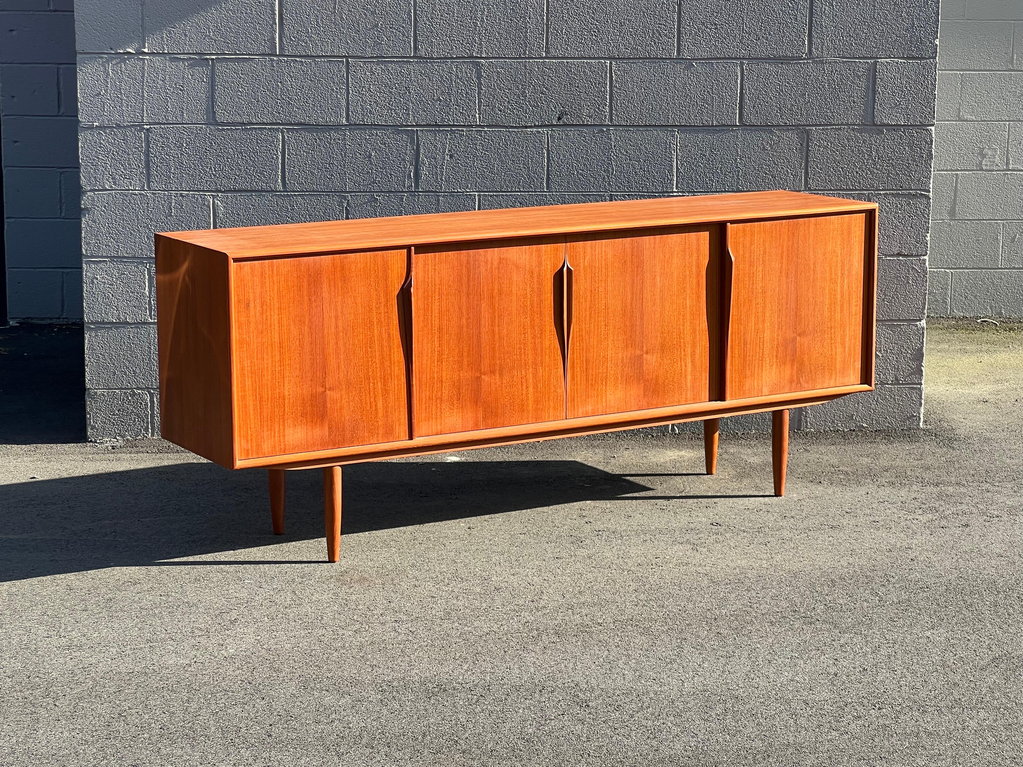 Danish teak credenza designed by Axel Christensen for ACO Møbler circa 1960s. This sideboard features four sliding doors with beautifully sculpted teak handles. Each compartment behind the doors opens to adjustable shelving and a total of four