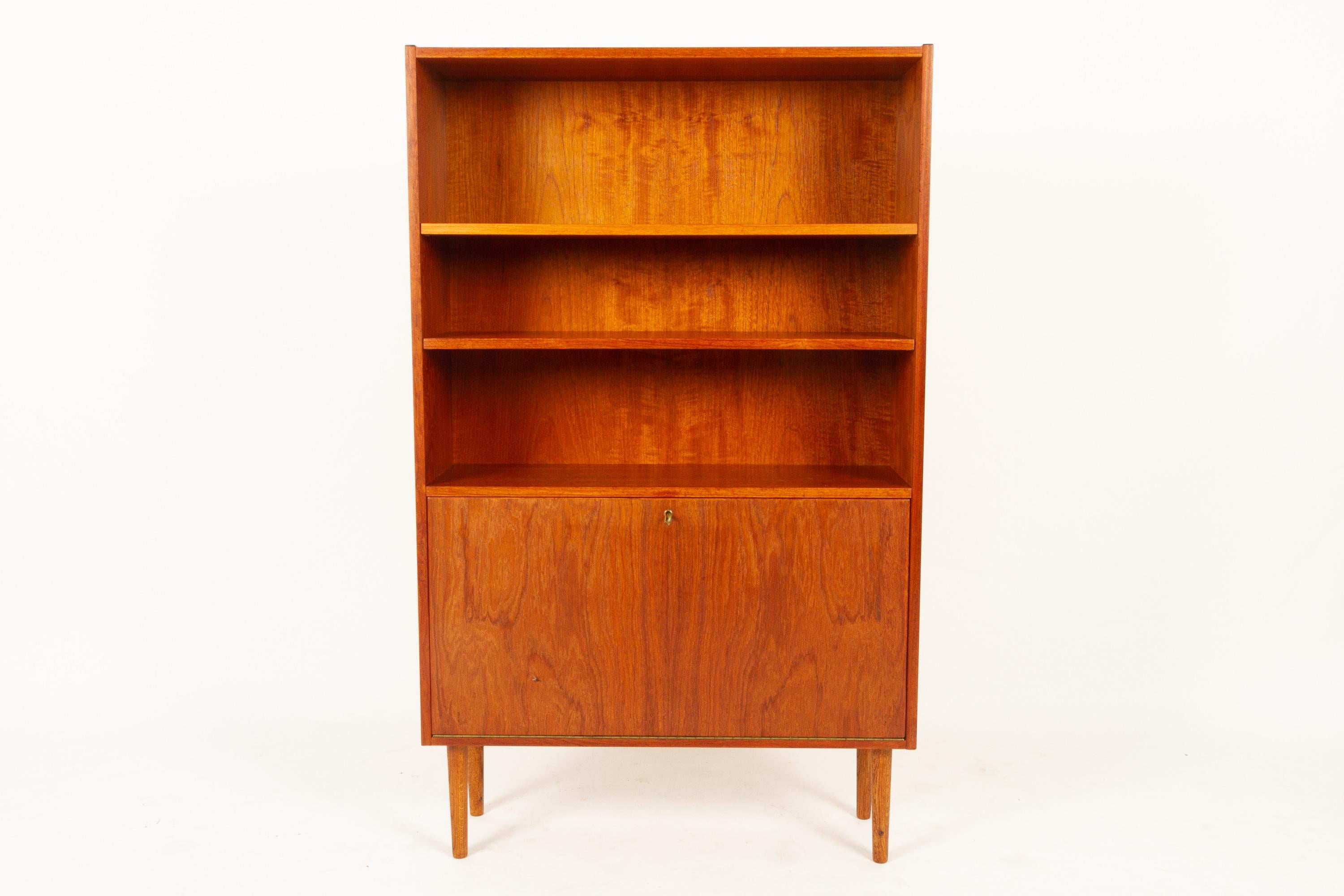Danish teak bookcase, 1960s.
Elegant slender bookcase in teak veneer. Two adjustable shelves and one cabinet with drop down door. Door has a lock with key. Standing on round tapered legs in stained oak (not original).
Good vintage condition,