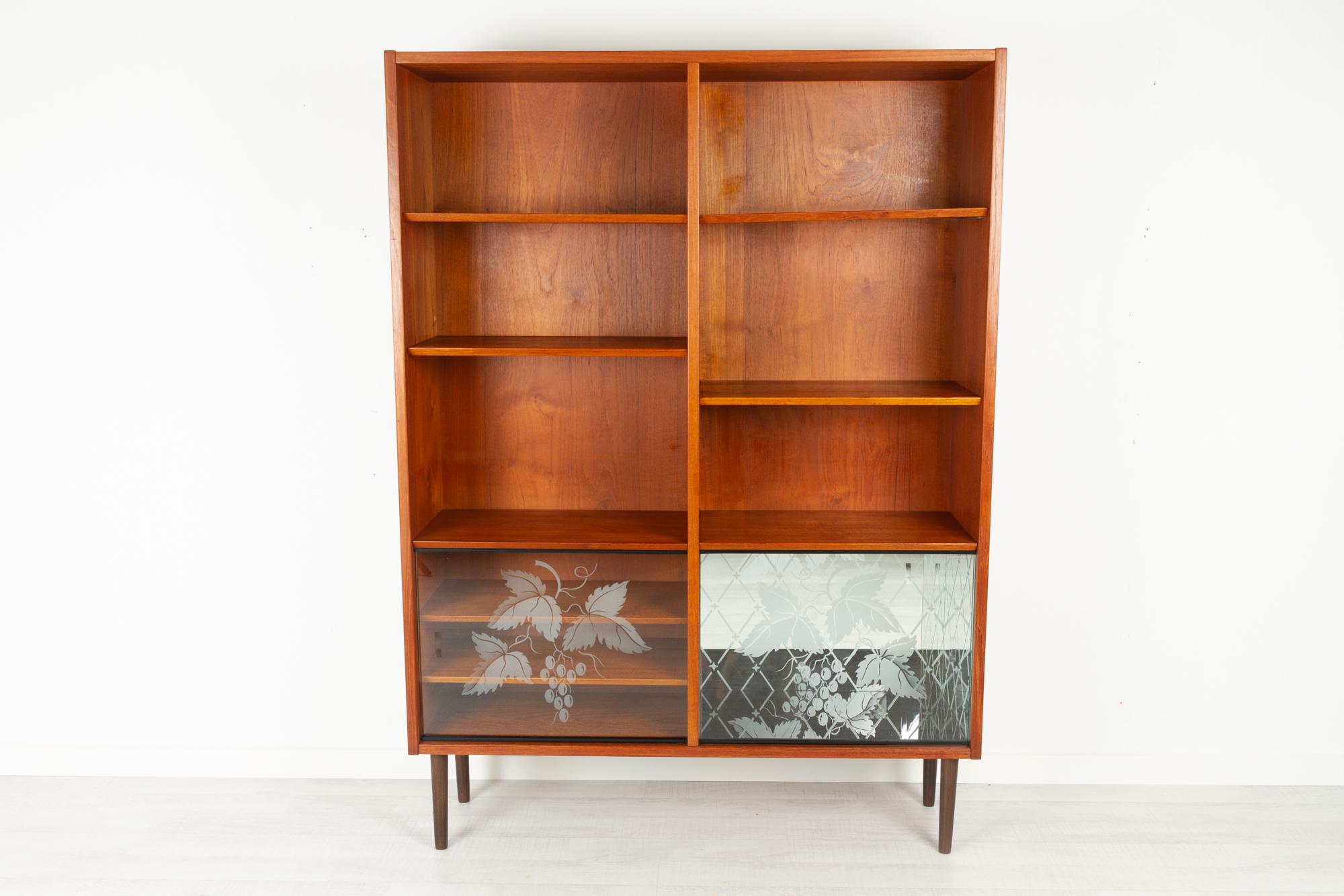 Vintage Danish teak bookcase by Hundevad & Co 1960s
Mid-Century Modern bookcase with mirrored dry bar unit and sliding glass doors. Glass doors has etched floral motifs. Six height adjustable shelves with slanted edge. Round tapered legs in solid