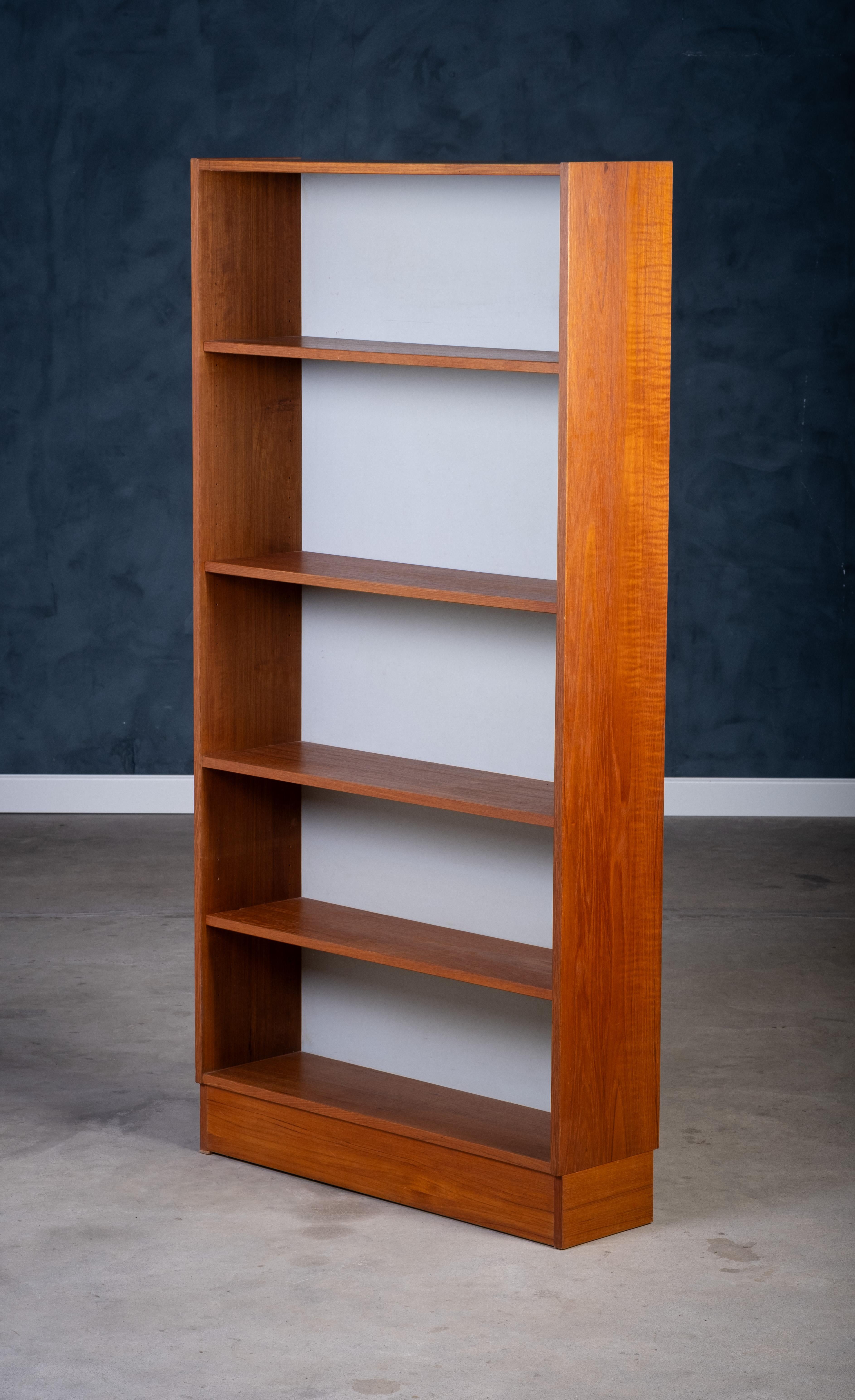 Spacieuse bibliothèque danoise des années 1960, produite par Domino, fabriquée en bois de teck chaud. Elle offre un espace de rangement généreux avec plusieurs étagères et un panneau arrière blanc/gris élégant qui met en valeur vos objets