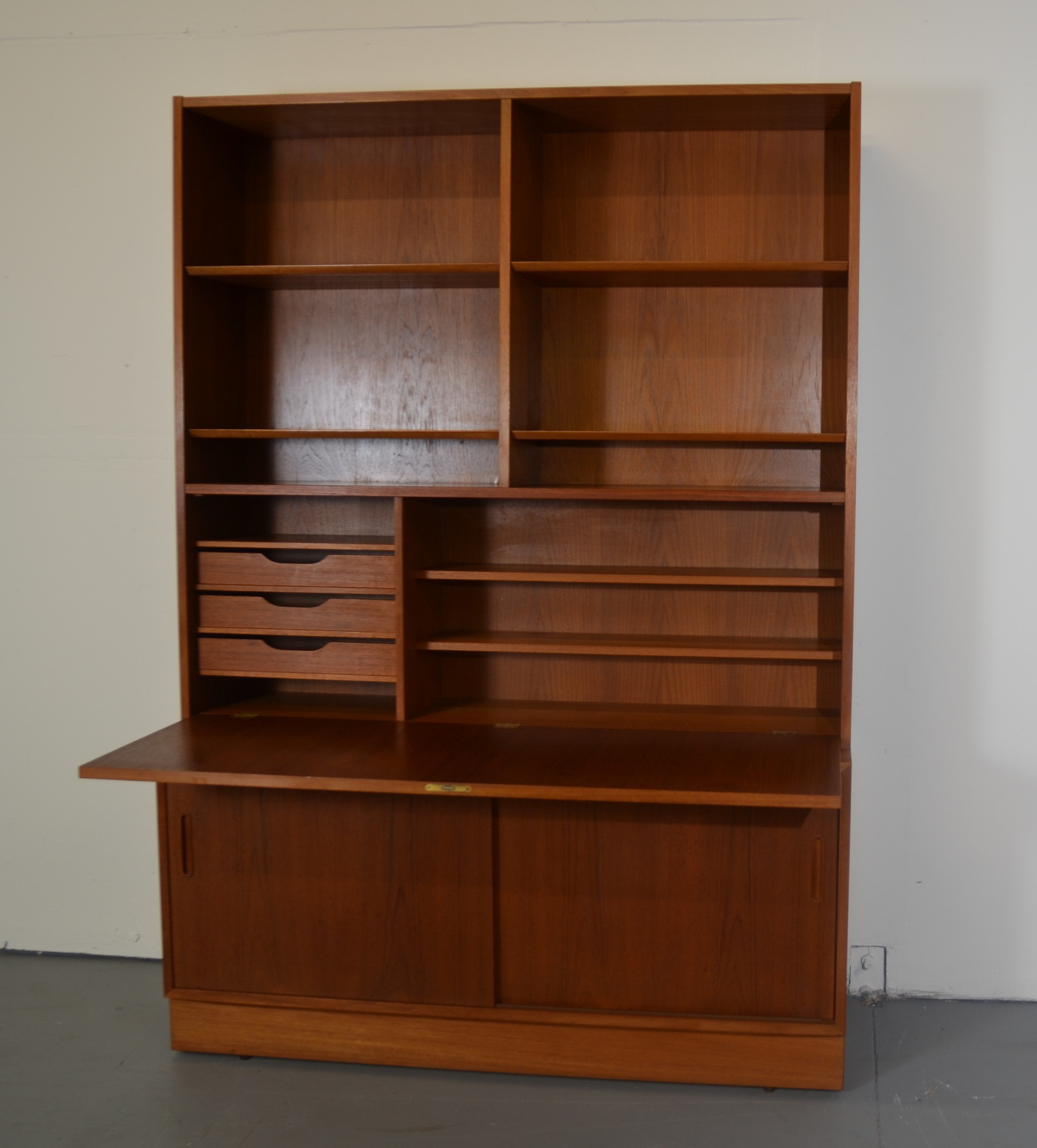 This gorgeous secretary was designed by one of the premier Danish Mid-Century designers, Poul Hundevad. As many of the mid-century designers were, Hundevad was inspired by the past for this piece with its drop front desk with bookcase above and