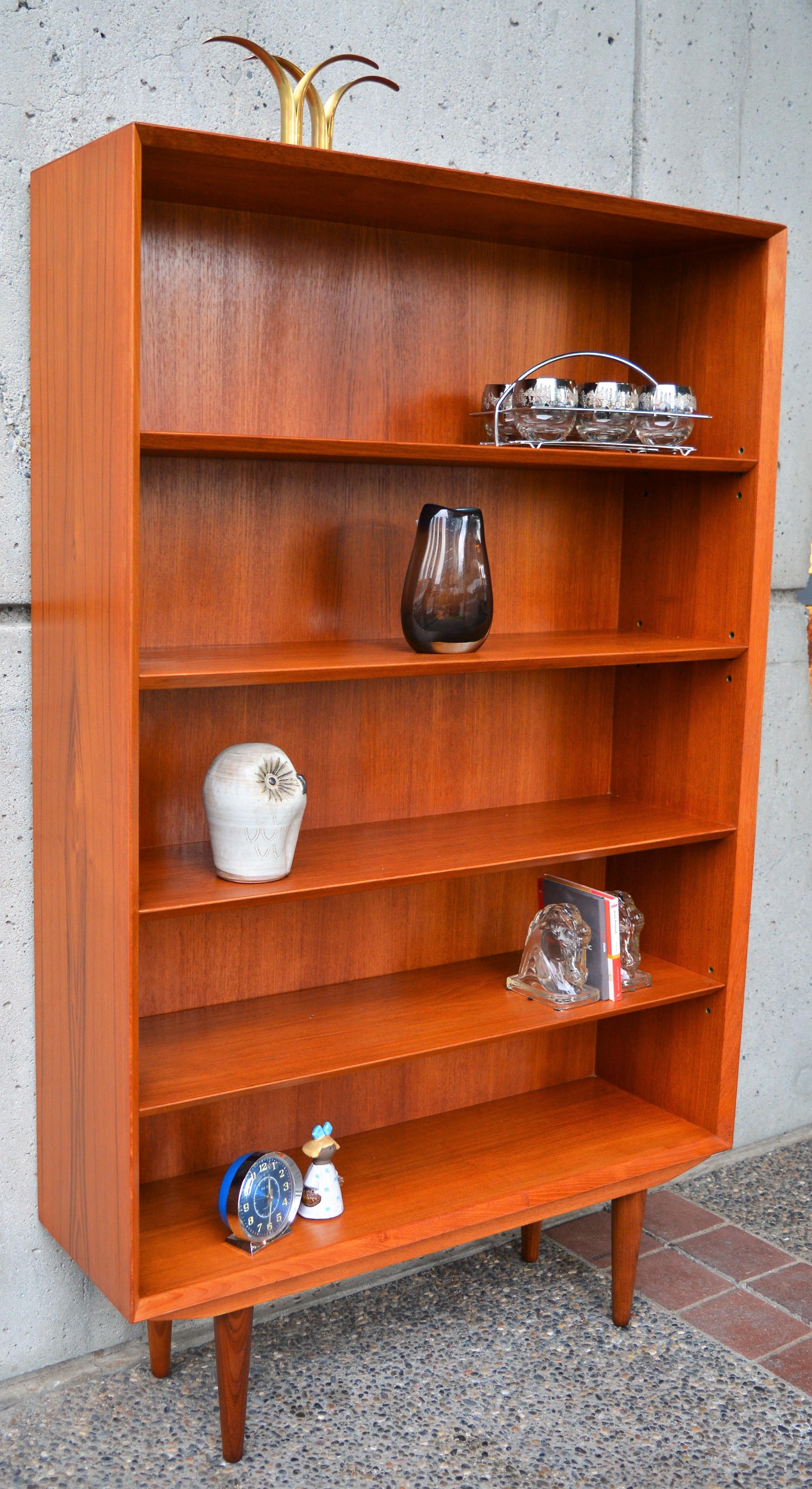 This fabulous and super unusual Danish modern teak book shelf is awesome! Featuring a mitered front molding detail that echoes the angled front edges of the shelves. Finished with substantial conical legs (removable for transport.) 3 of the shelves