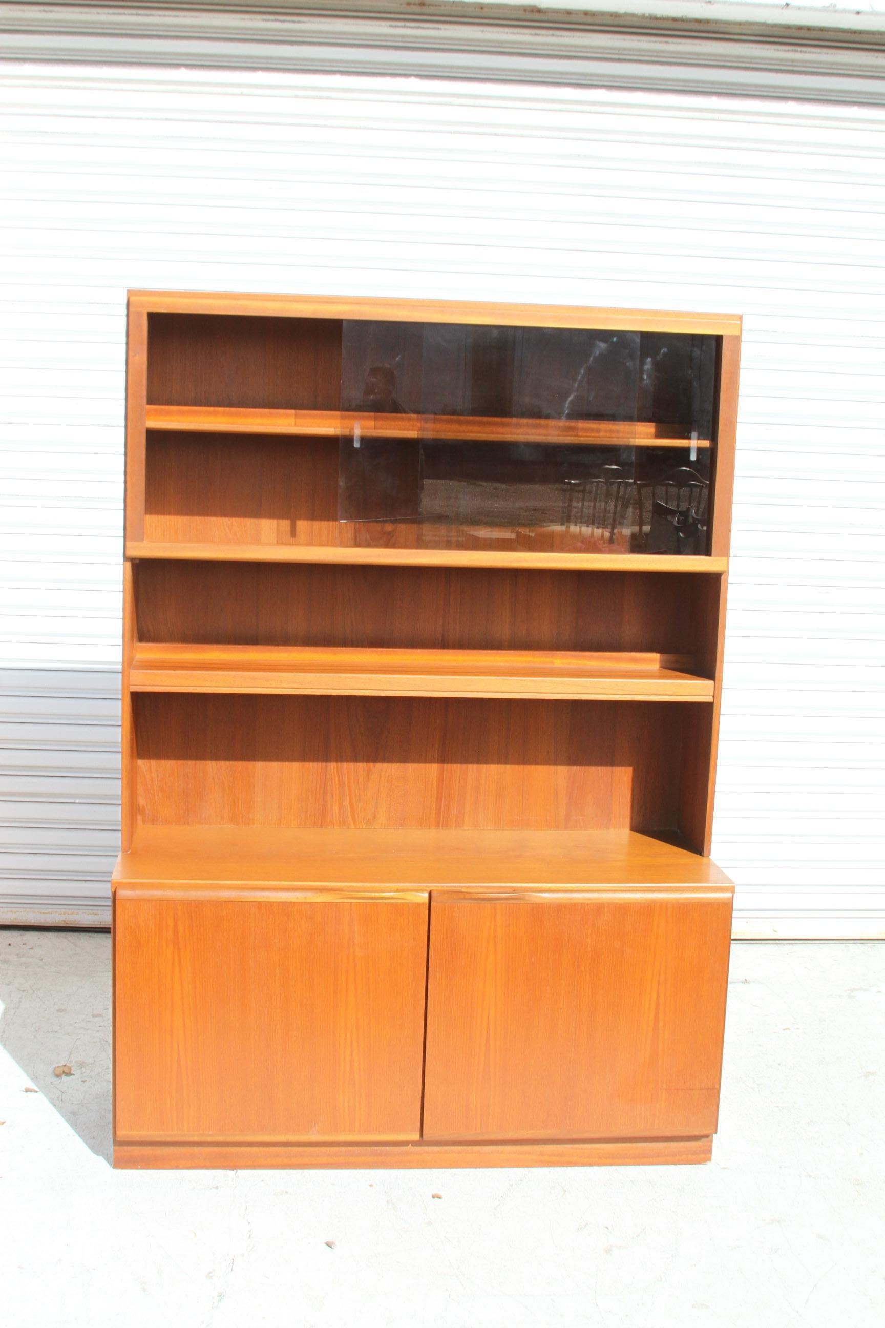 Questa libreria in teak è molto capiente. La parte superiore è dotata di 4 ripiani per ospitare molti libri e oggetti d'arredamento. La parte inferiore è dotata di due ante che offrono un ampio spazio per il mobile. L'unità è realizzata in