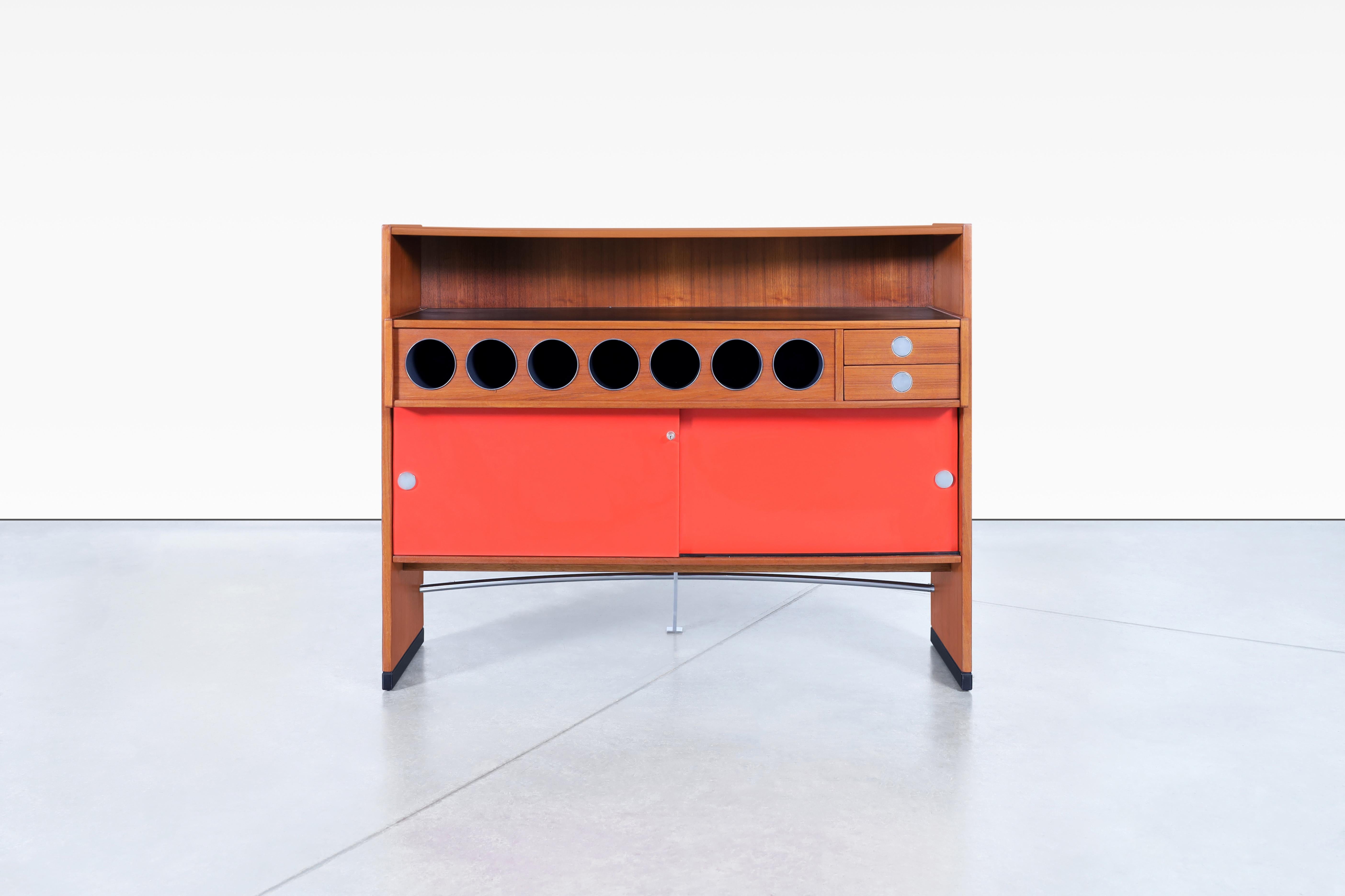 This Danish teak boomerang dry bar by Erik Buch for Dyrlund is a stunning piece from the 1960s. Its striking boomerang-shaped front and chrome-plated steel footrest exude mid-century modern charm. The back features a straight extension, creating a