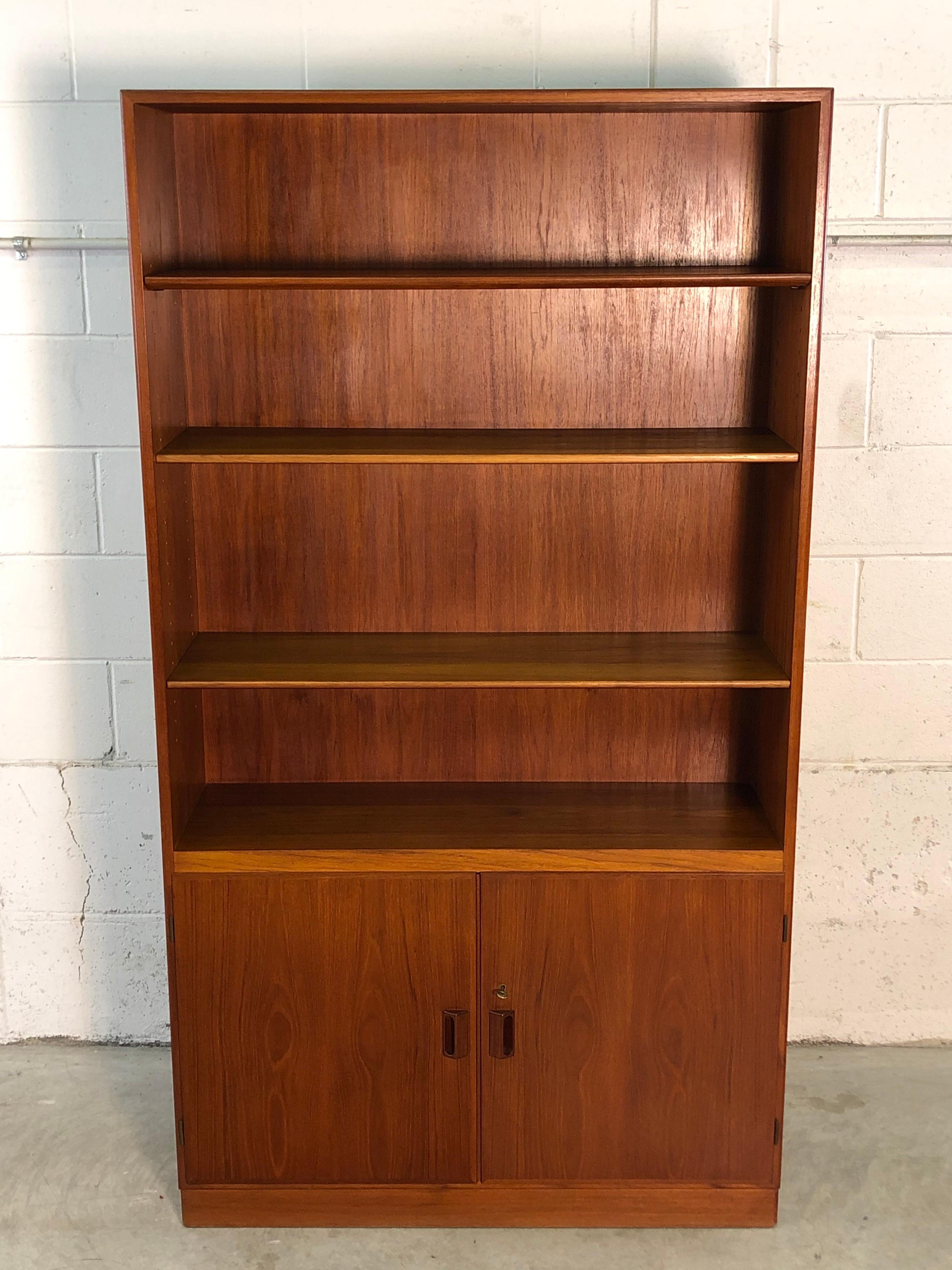 Vintage Danish teak tall bookcase cabinet designed by Børge Mogensen for Povl Dinesen Furniture Co. The bookcase has three adjustable shelves on top and one adjustable shelf underneath. Great Mogensen designed pulls and comes with the key that locks