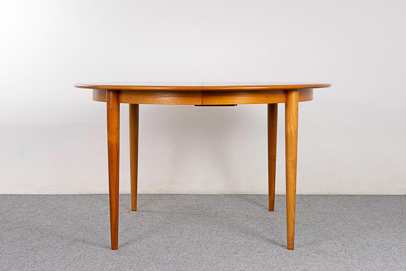 Teak mid-century dining table, circa 1960's. Lovely bookmatched veneer top, generous solid edging & sleek, elegant tapering legs. Cozy, social circular shape is perfect for 4 people. Add leaves to seat up to 8! Self storing drop down leg adds