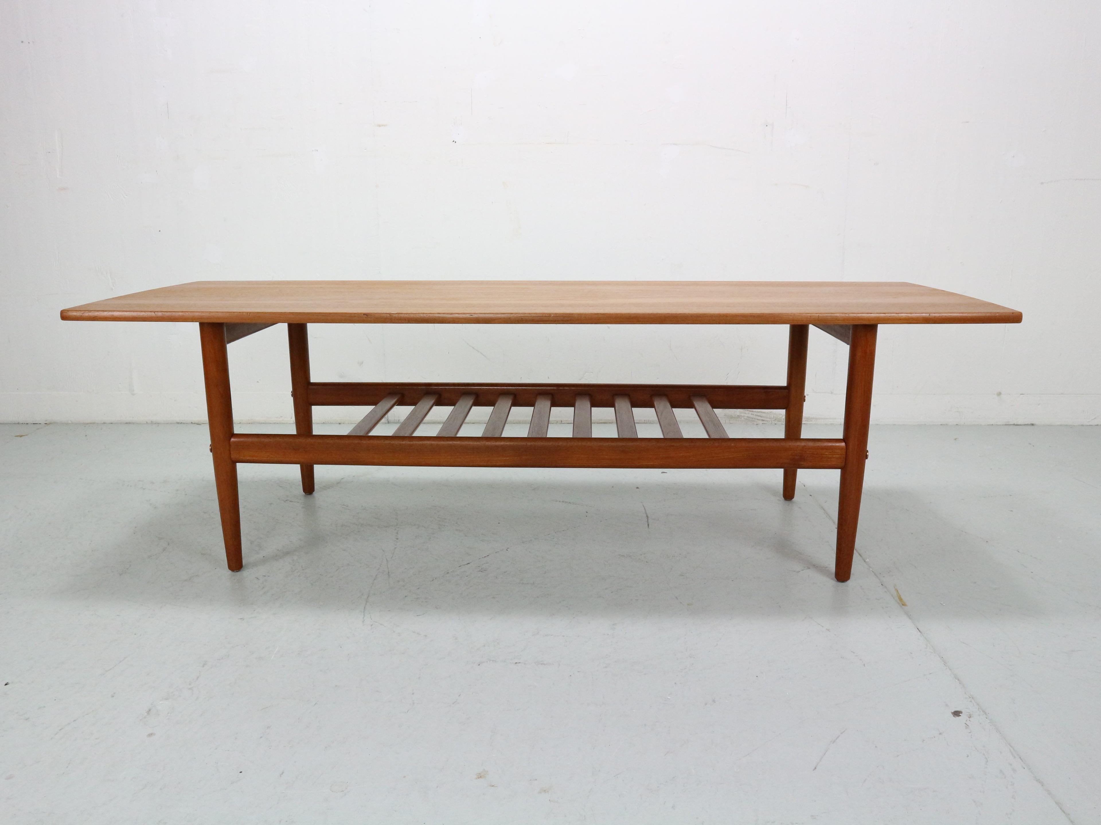 A stunning mid-century modern, teak Danish coffee table by Grete Jalk for Glostrup Mobelfabrik, circa 1960's. Features a rectangular top with an unique slatted lower level floating shelf adds additional space for storage. The table rests on stylish
