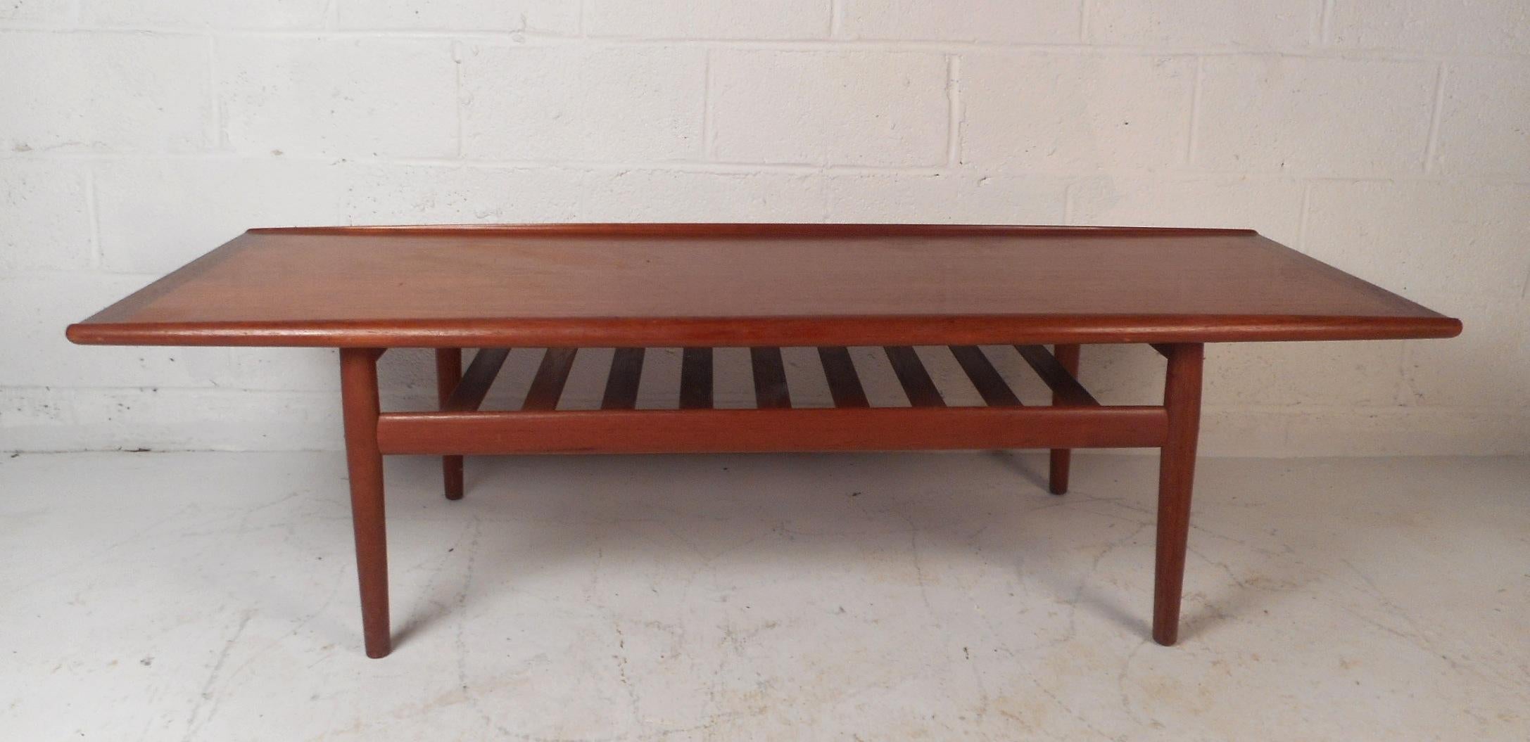 This beautiful turned edge coffee table by Grete Jalk is the perfect vintage blend of Danish modern design. Stunning teak finish, shapely design, and stretchers for added sturdiness. A unique slatted lower shelf adds additional space for storage