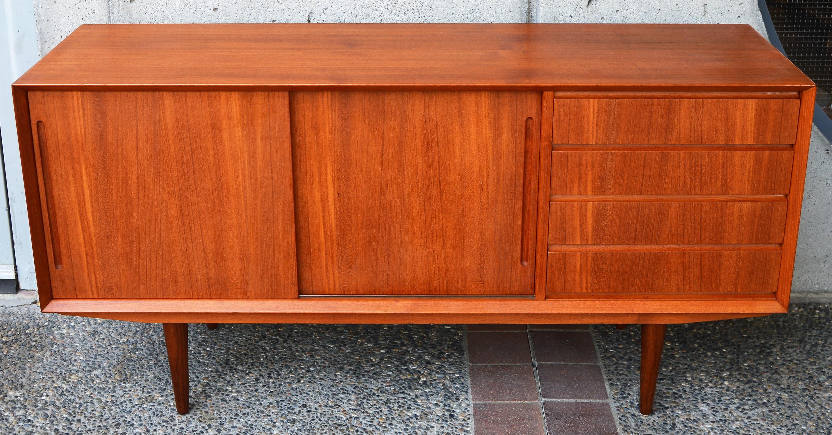 This hot Danish modern mid-size teak credenza or buffet was manufactured by Alderslyst Mobelfabrik, Denmark, in the 1960s. Featuring an asymmetrical bank of drawers on the right, with continuous grain down the drawer fronts, elongated carved drawer