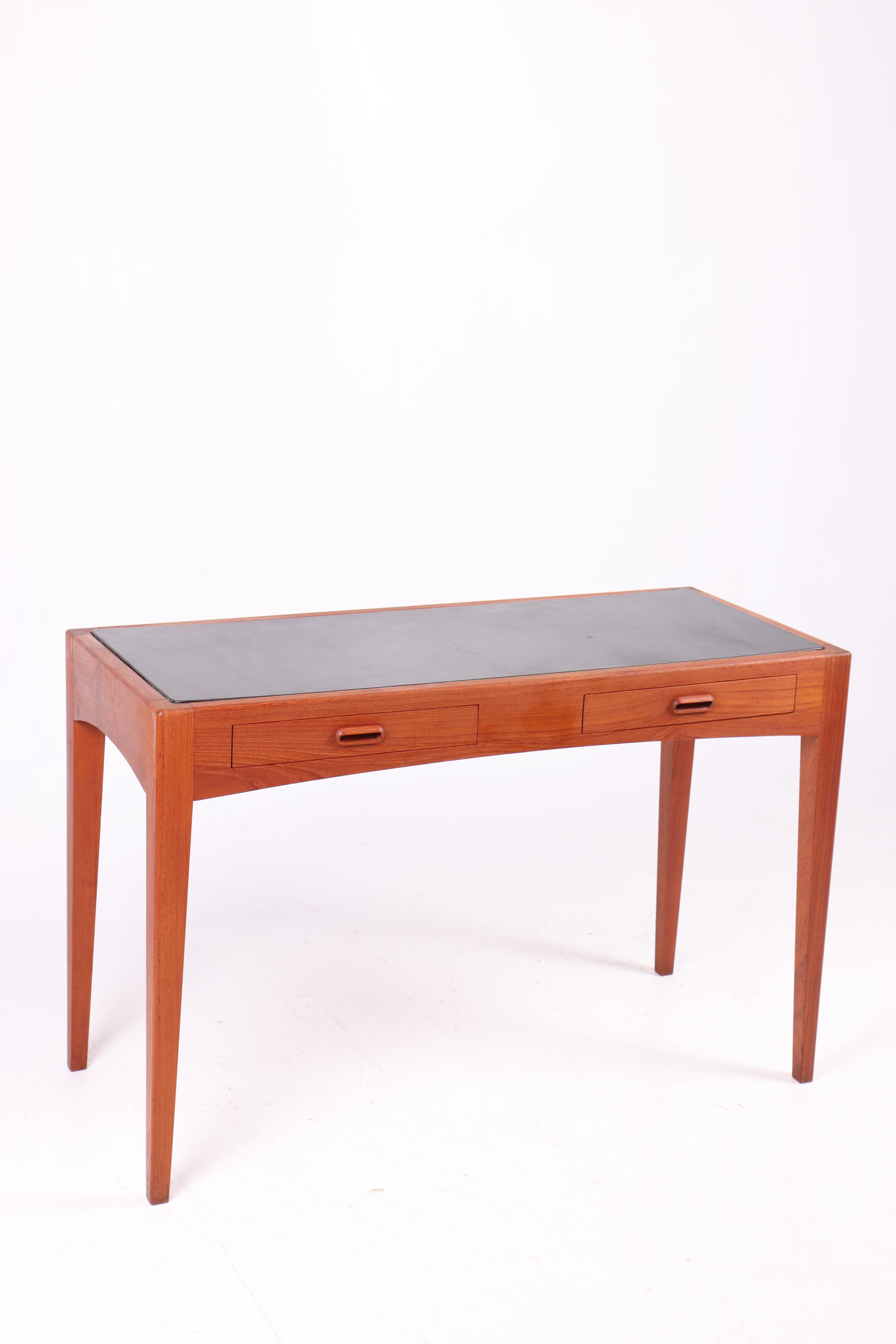 This console table from the 1960s is produced in Denmark and crafted from teak wood with a leather-covered tabletop, adding a sophisticated and elegant touch to its minimalist design. The console features two drawers with integrated handles,