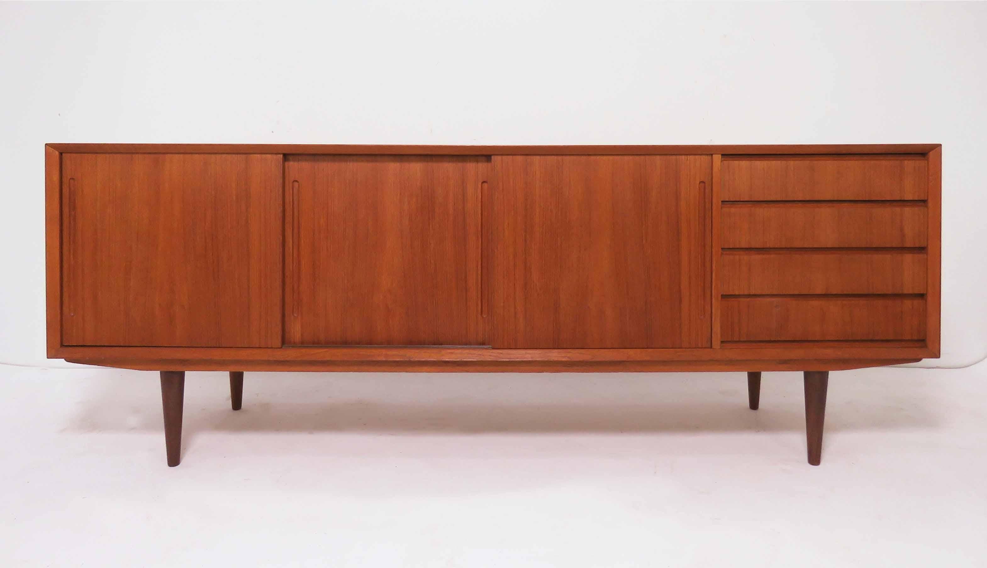 Classic teak credenza by Alderslyst Mobelfabrik, made in Denmark, circa 1960s. Book matched door and drawer fronts. Shallow drawers to the right including one felt lined for silverware storage; shelving storage behind the sliding doors to the left.