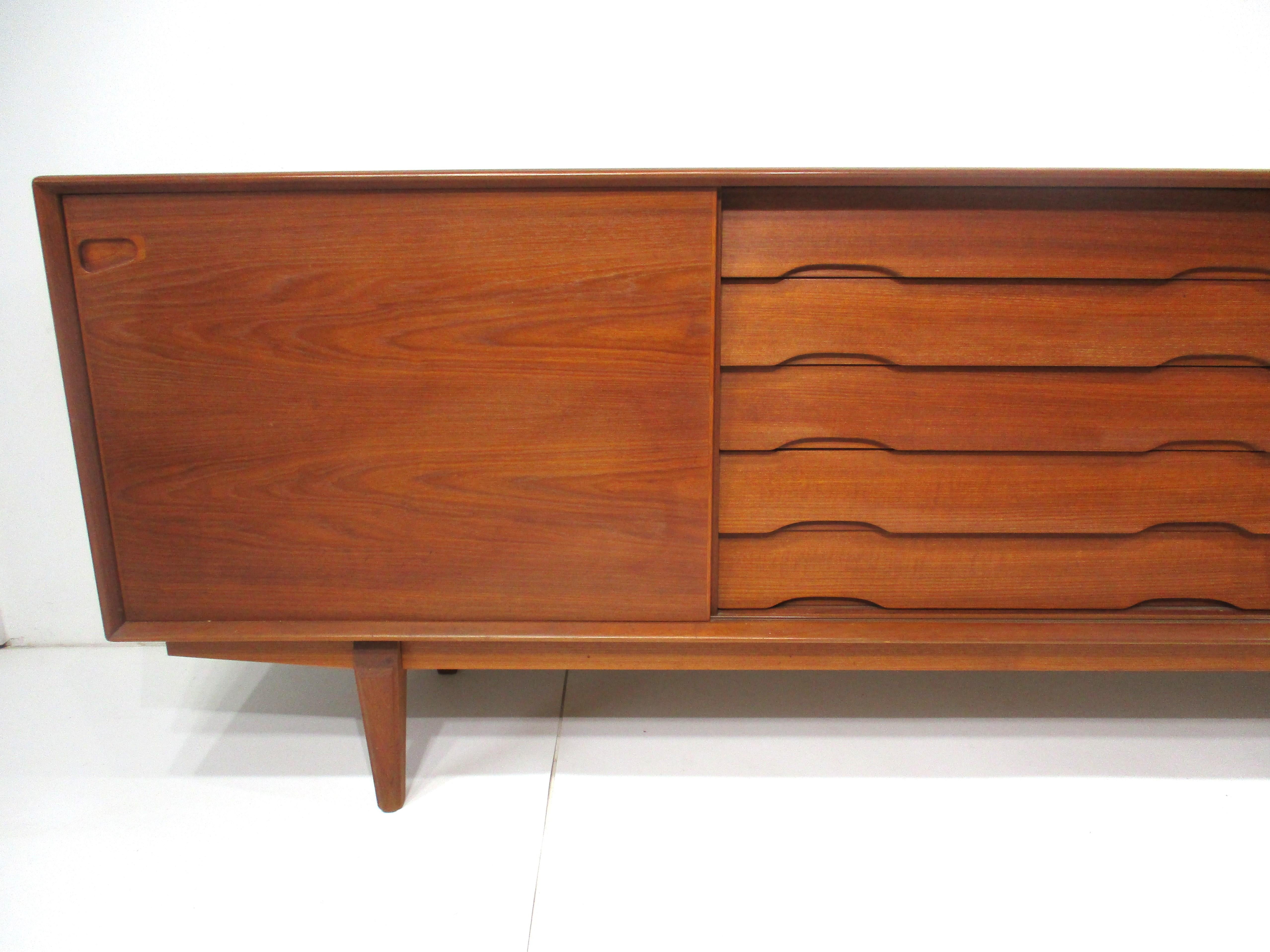 A very well crafted teak wood credenza with five center drawers and cut out lower handles and inset door pulls . A sliding door to each end with the left side having one adjustable shelve and the other two adjustable shelves giving you plenty of