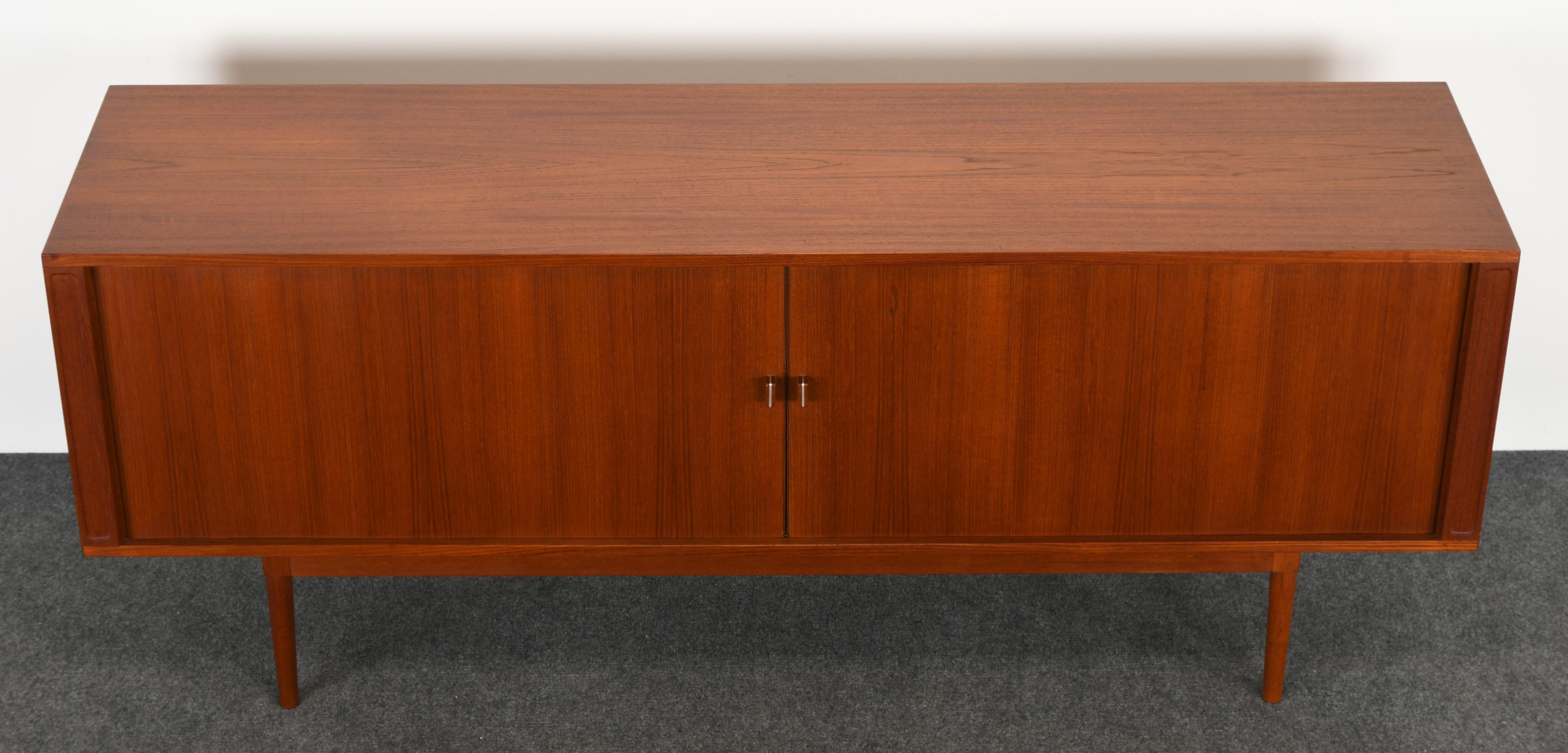 A handsome teak credenza designed by Jens Quistgaard for Peter Lovig. This teak sideboard has two tambour doors that reveal five shelves and five drawers for ample storage. The cabinet has a tapered leg base and finished back so it can be displayed
