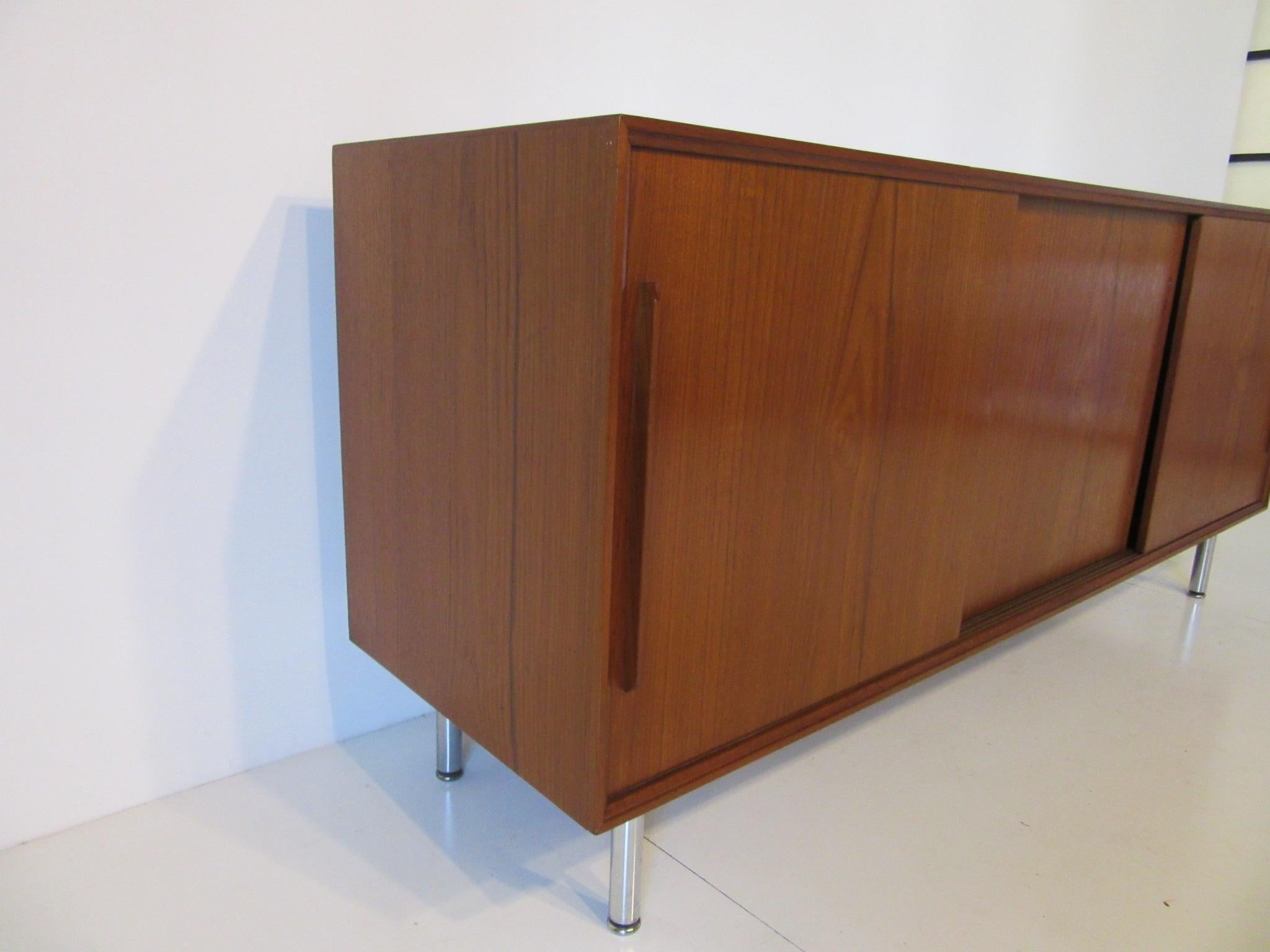 A three sliding door teak wood credenza or server with adjustable shelves, two small drawers to one side and plenty of storage sitting on rounded chrome legs. Made in Denmark by Skovby Mobelfabrik AS.
