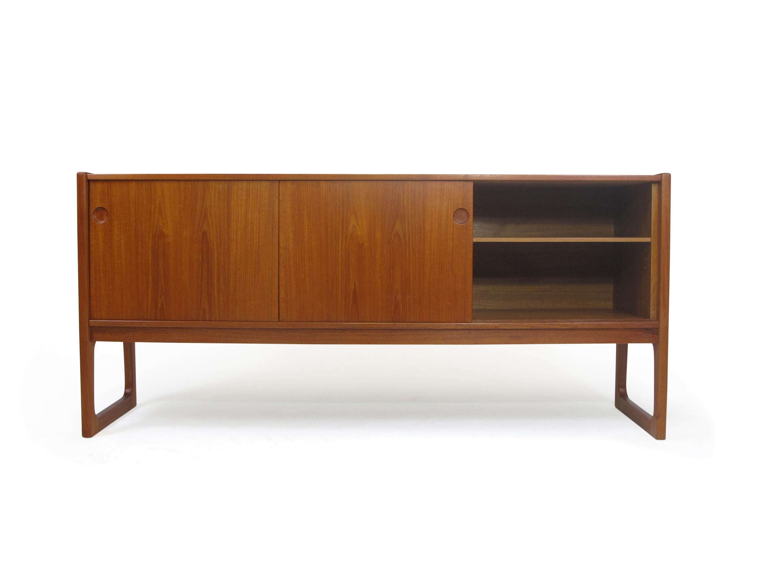 Mid-century teak credenza attributed to Gunni Oman, Denmark. Crafted of teak with book-matched grain and recessed pulls. The cabinet has two sliding doors, three drawers in the center, with adjustable interior shelves, and finished on the back.