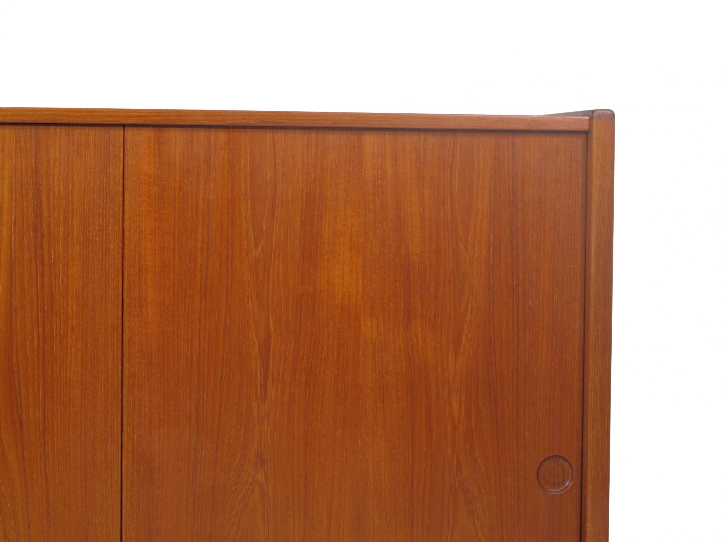 Mid-century Teak credenza designed by Omann Jun with three sliding doors with book-matched grain and recessed pulls, revealing an interior with adjustable shelves, and silverware drawers on the left side. Raised on round tapered legs.