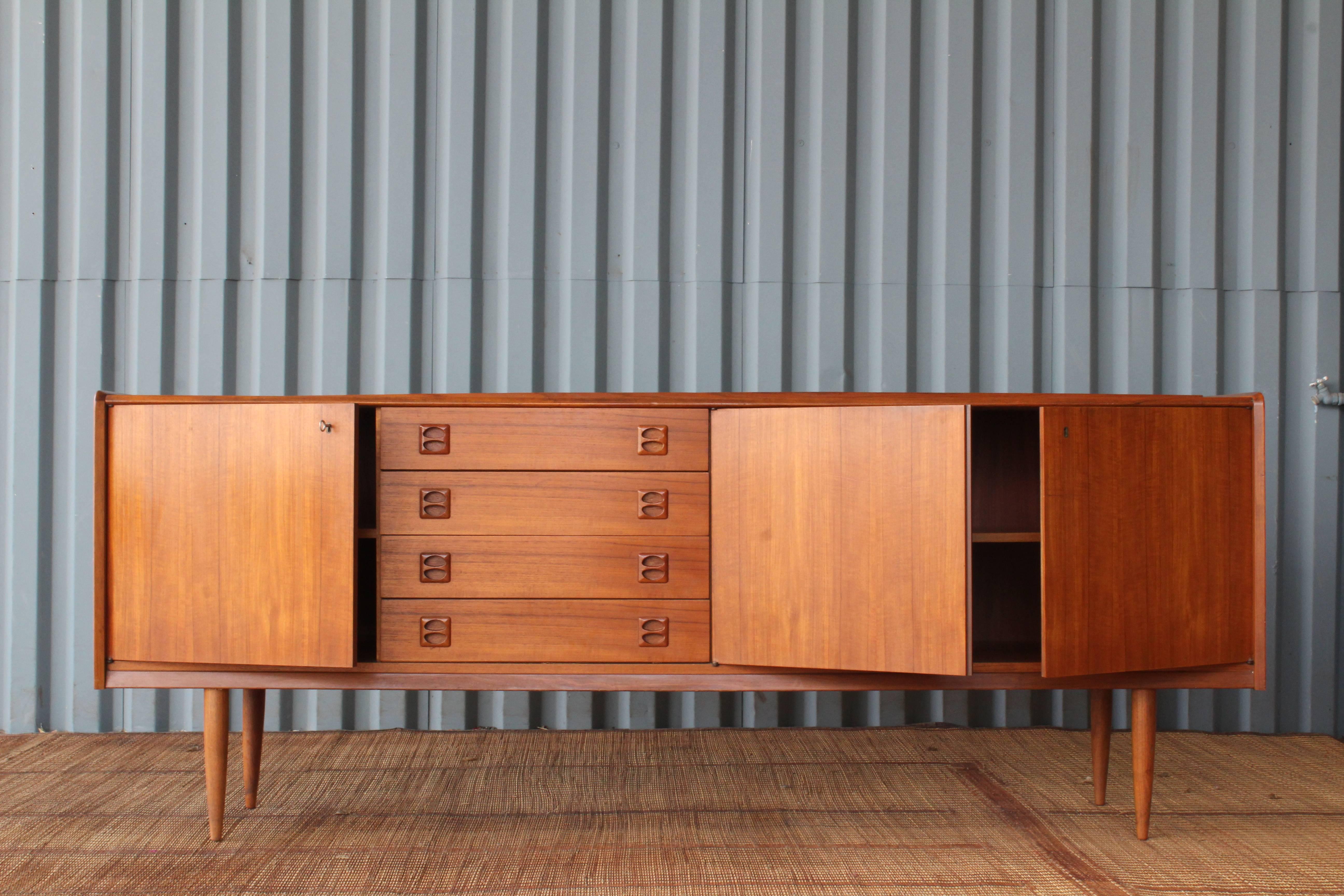 1960s Danish teak credenza. Features two locking doors with the original key and four drawers with sculpted teak pulls.