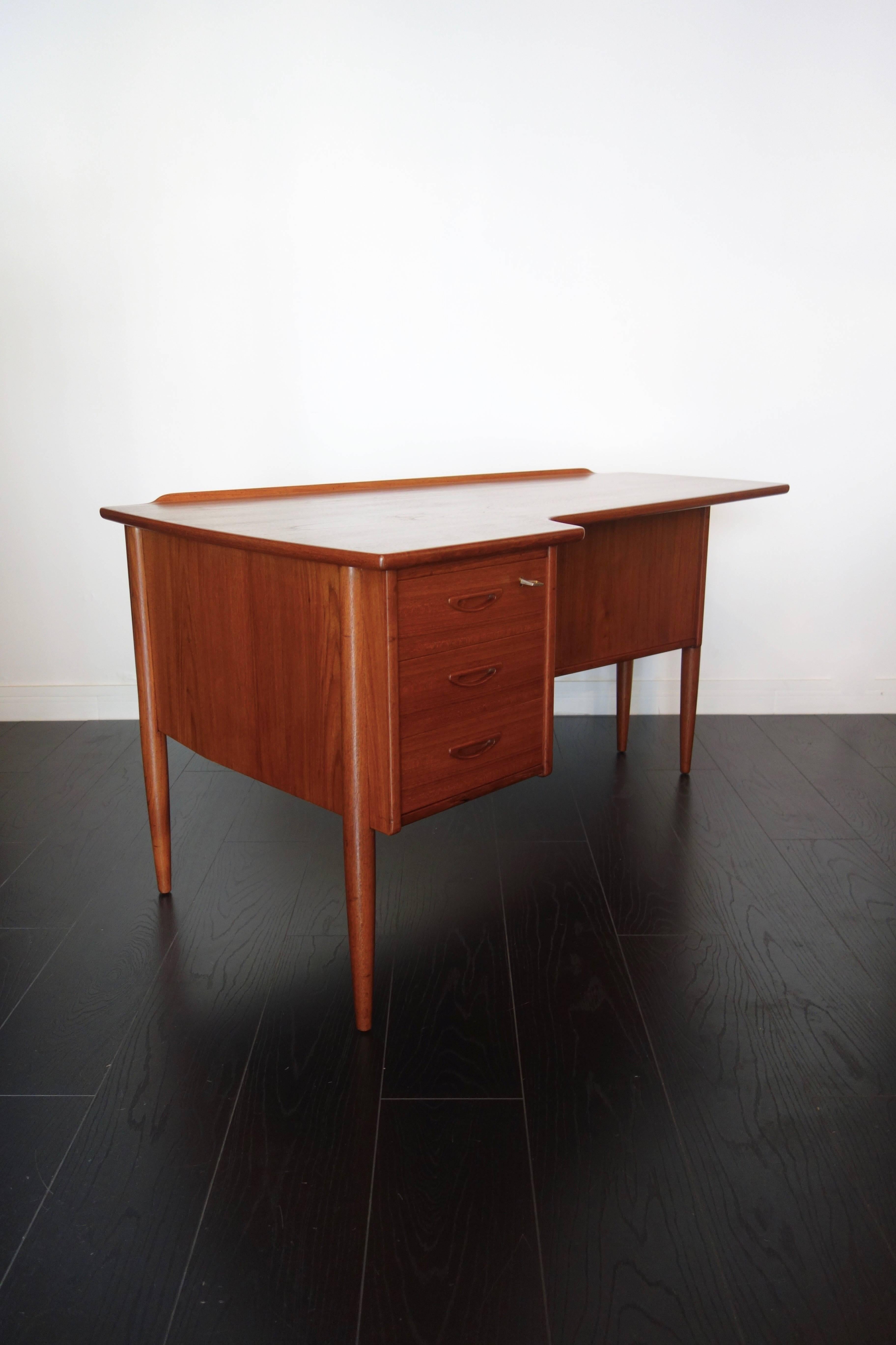Double teak desk by Peter Løvig Nielsen. Made in the 1960s Danish. Boomerang shape, tapered round legs, three drawers with inlaid handles, recess and cupboard at the back with removable shelf. Keys and locks of origin. In exceptional condition: