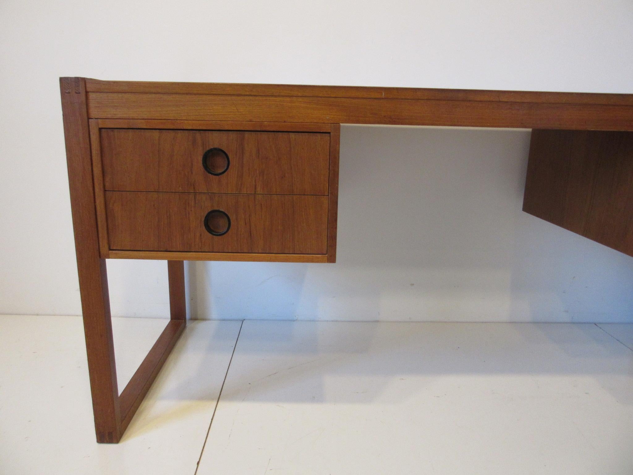 A nice sized desk for home or office made of teak, well constructed and sturdy having finger jointed legs having four drawers with round inset black pulls. Designed in the manner of Henning Jensen Torben and Valeur made in Denmark.